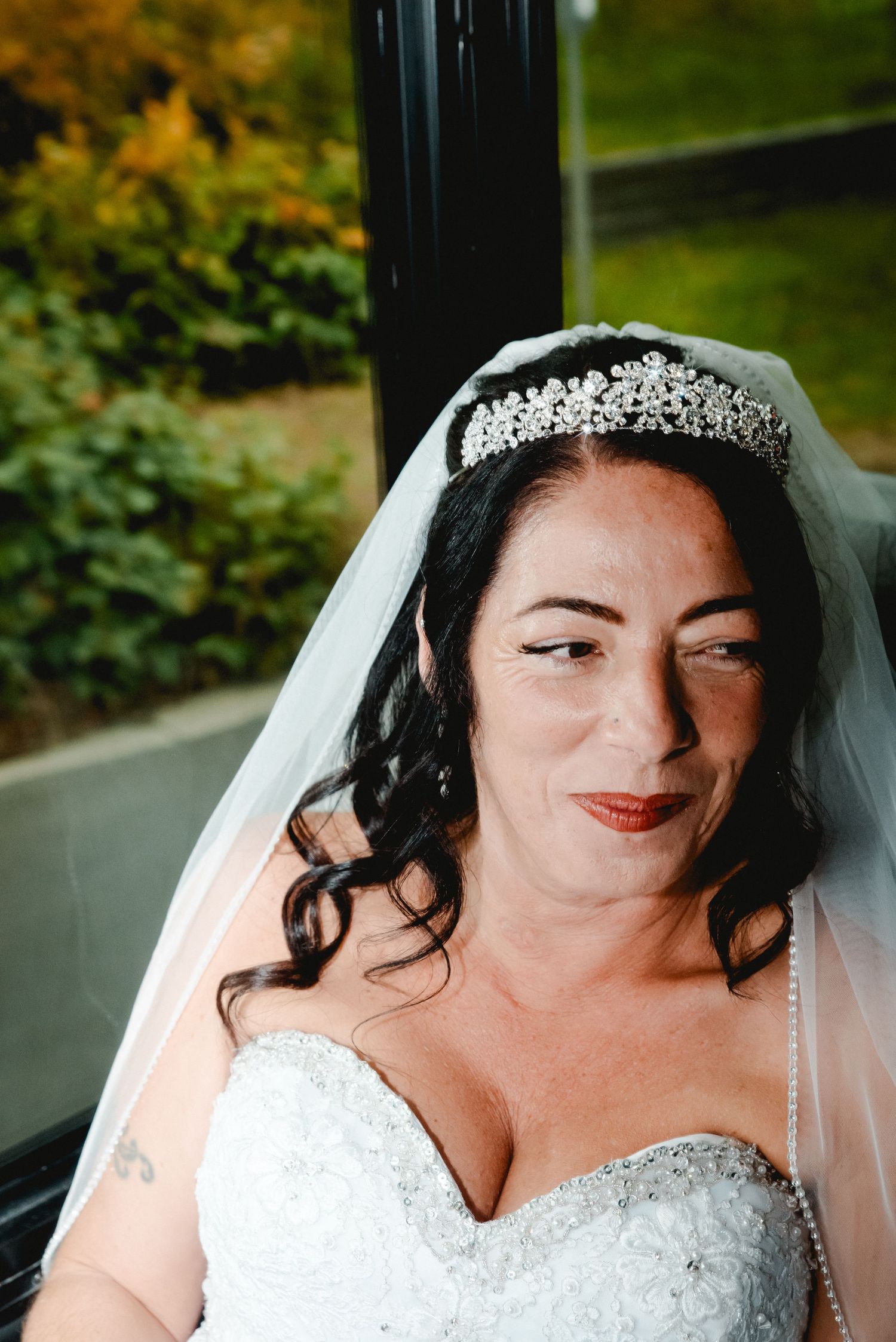 A stunning close up of the bride smiling. You can see the details on her dress and tiara and fall colors out the window of the party bus.