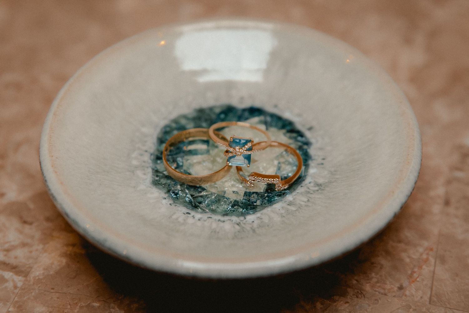 Gold and aquamarine wedding rings on a sparking blue and white plate, taken close up to show off the ring's details. Taken in New York.