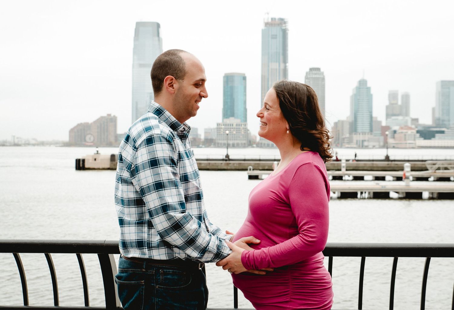 A pregnant woman and her husband hold hands and look into each others eyes smiling on a spring morning in New York City.