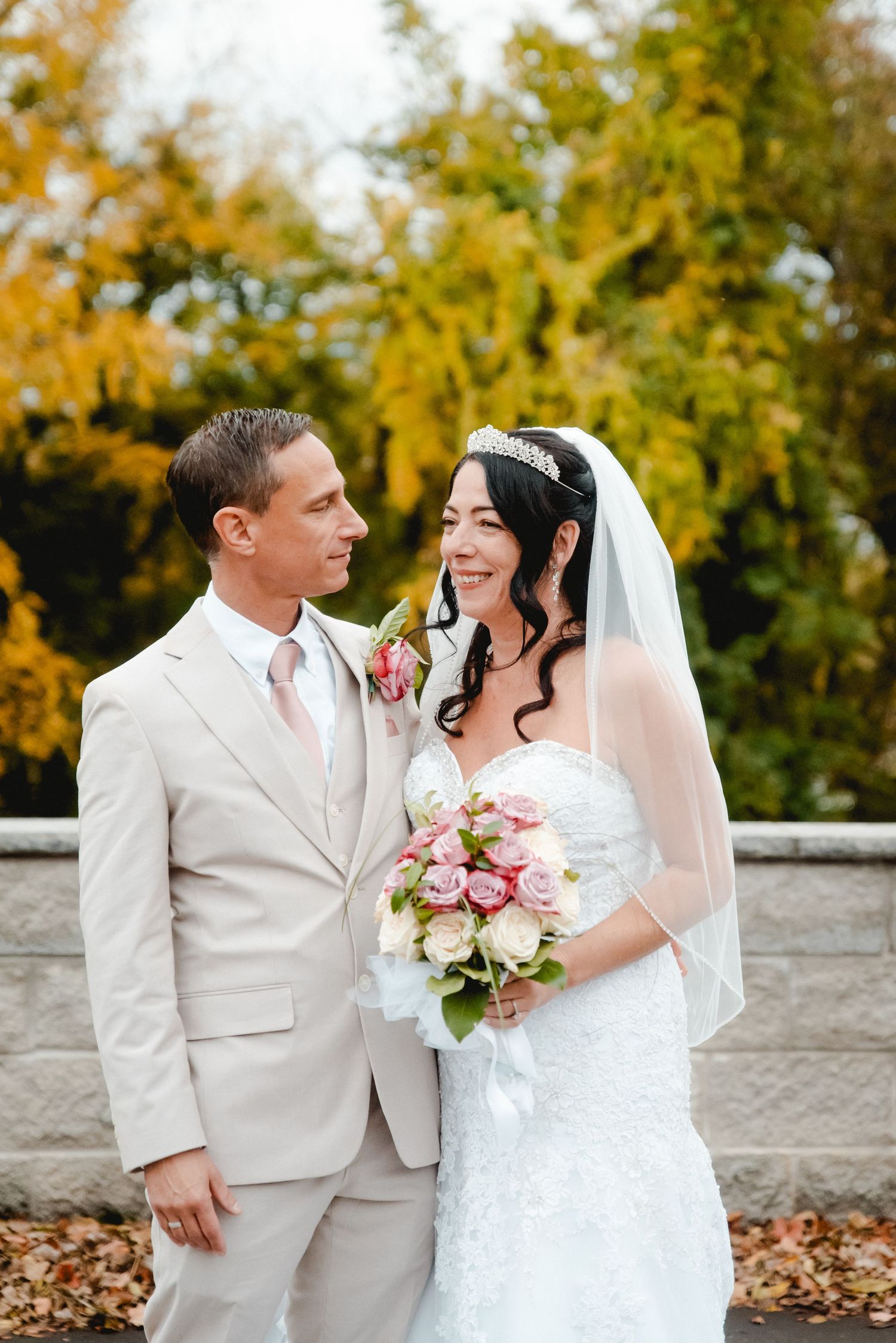 The bride and groom look at each other smiling while taking portraits after their wedding ceremony on a fall day in Vestal, New York.