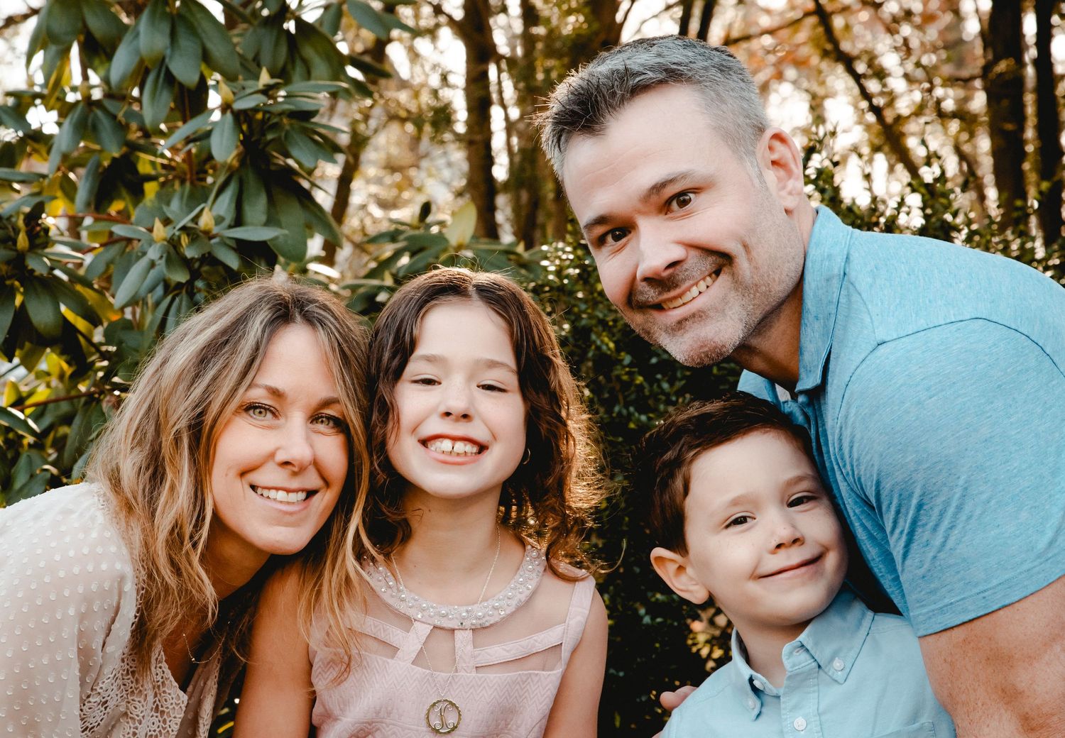 A family portrait in Westchester, NY. Everyone smiles and laughs while looking at the camera. Glowing sunlight & trees in the background