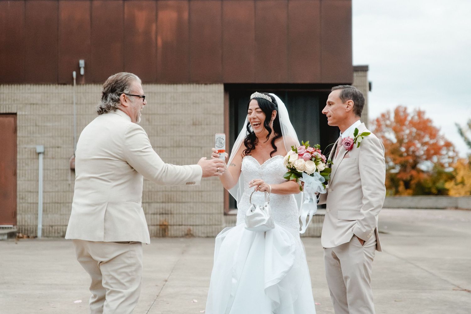 The best man brings a drink to the bride and groom after their fall wedding ceremony in Vestal, NY. Everyone is smiling and laughing.