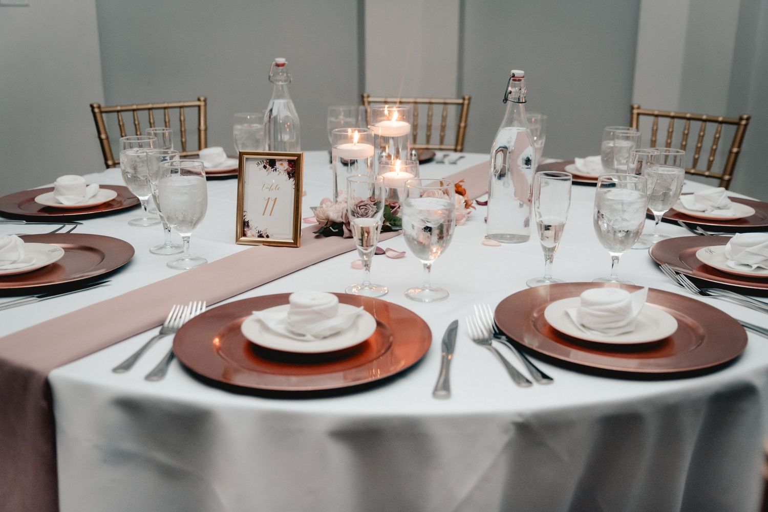 A guest table for a wedding at Riverdale in Endicott, NY. The table is set with beautiful rose gold cutlery, flowers, and candles.
