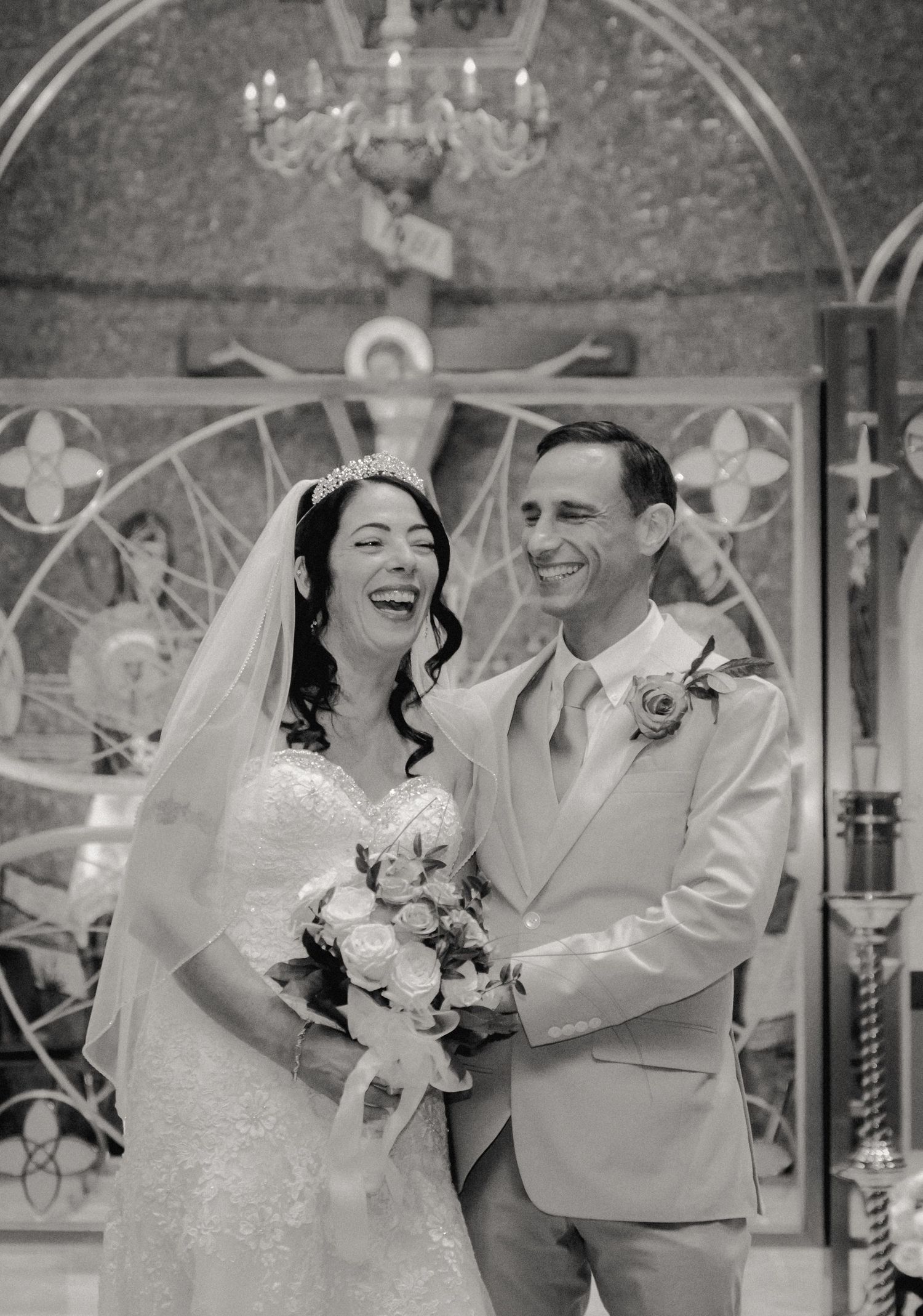 While taking portraits after their church ceremony, the bride and groom share a laugh captured in a timeless black-and-white photograph.