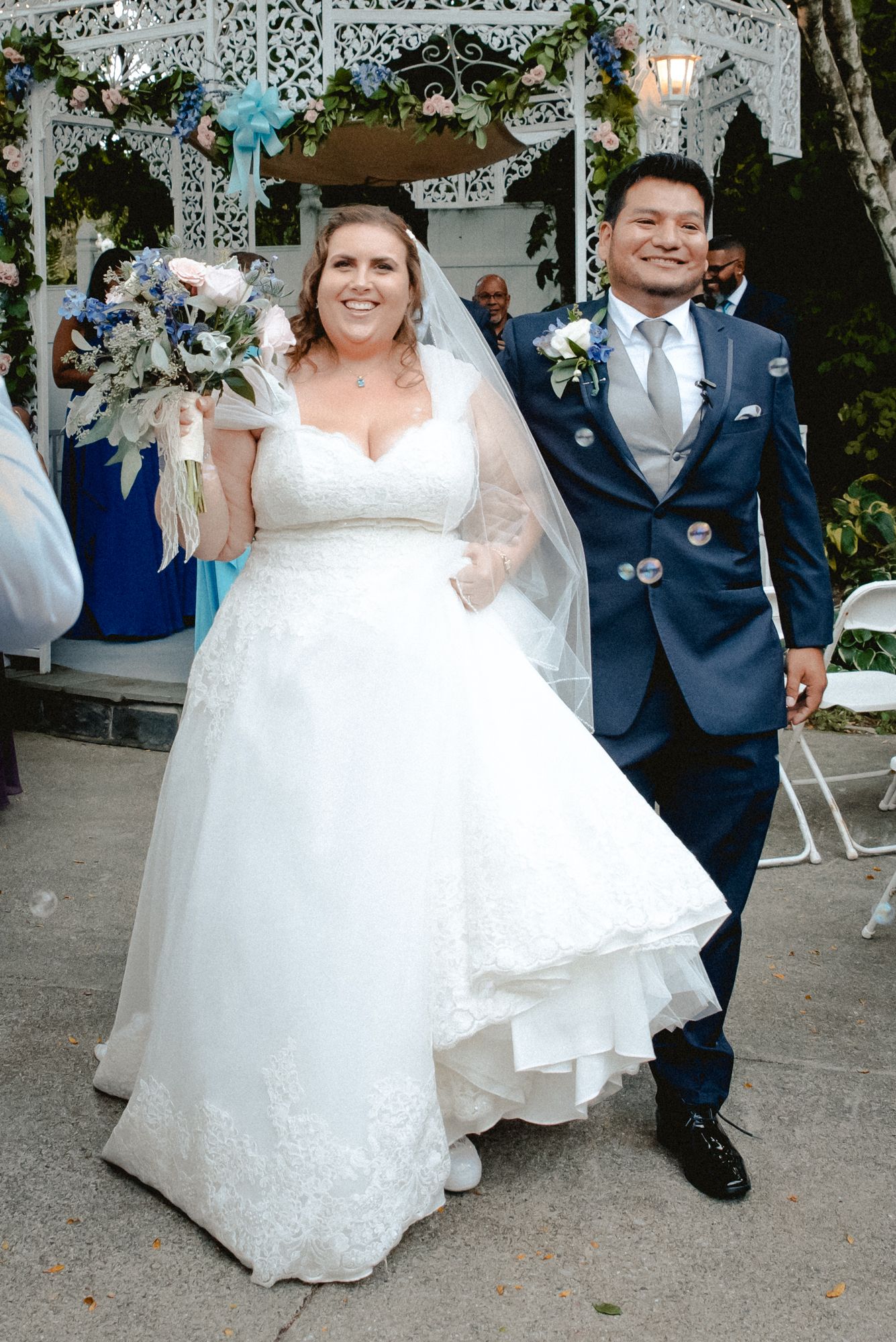 The bride and groom walk down the aisle together as husband and wife affer the ceremony. The bride holds up her bouquet in celeration.