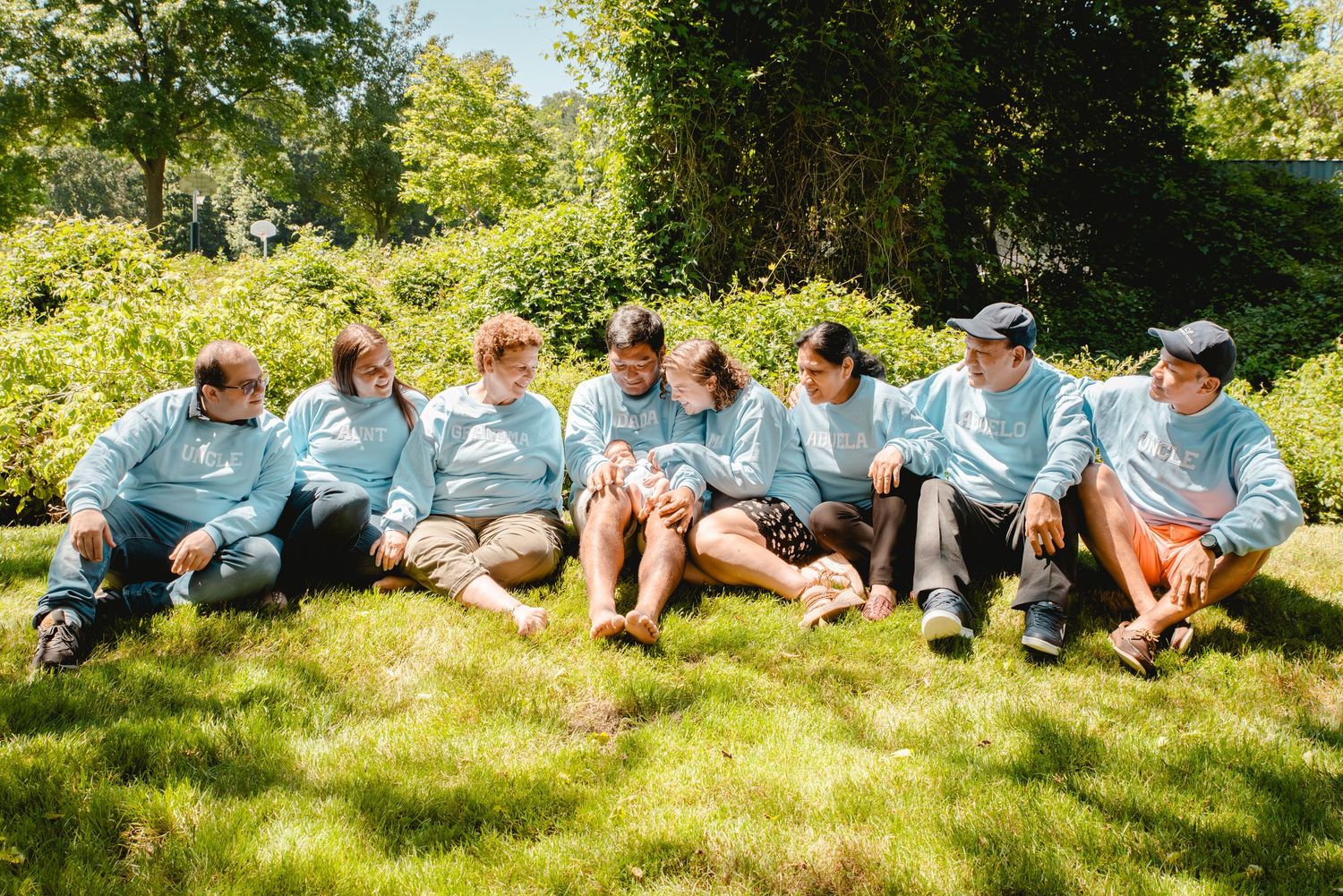 Three generations of family in matching outfits gather under a tree to welcome a baby boy in Westchester, NY.