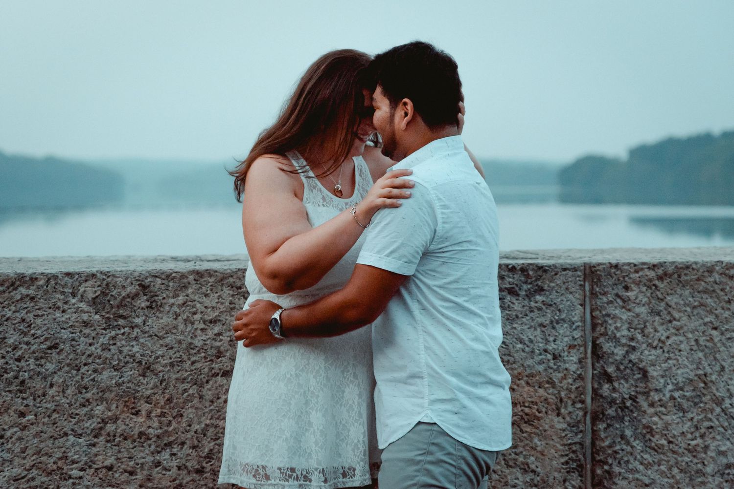 A newly engaged couple embrace while touching foreheads at the Kensico Dam Plaza in Valhalla, NY at dusk.
