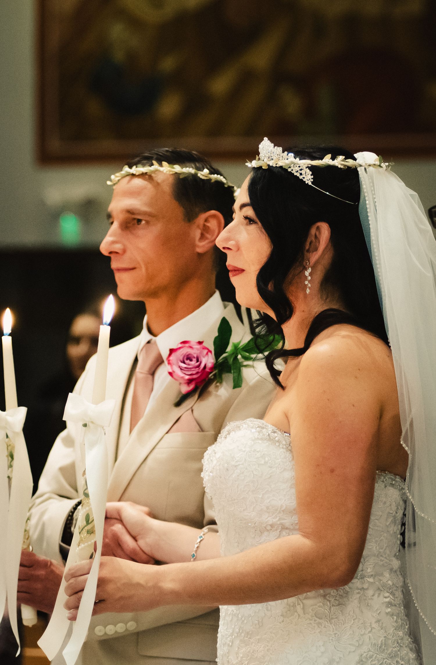 The bride and groom stand at the alter in their church, each holding a single tapered candle. The light is glimmering in their eyes.