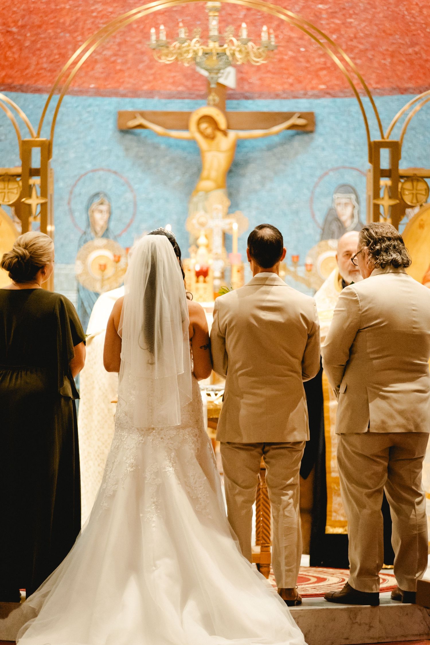 The bride and groom standing at the altar, photographed from behind as they prepare to make their vows to one another. Taken in a church.