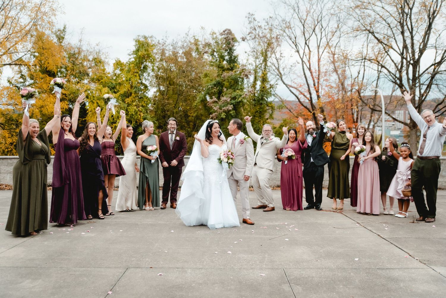 The bride and groom smile as the wedding party surrounds them, cheering and celebrating after their beautiful fall ceremony in Upstate NY.