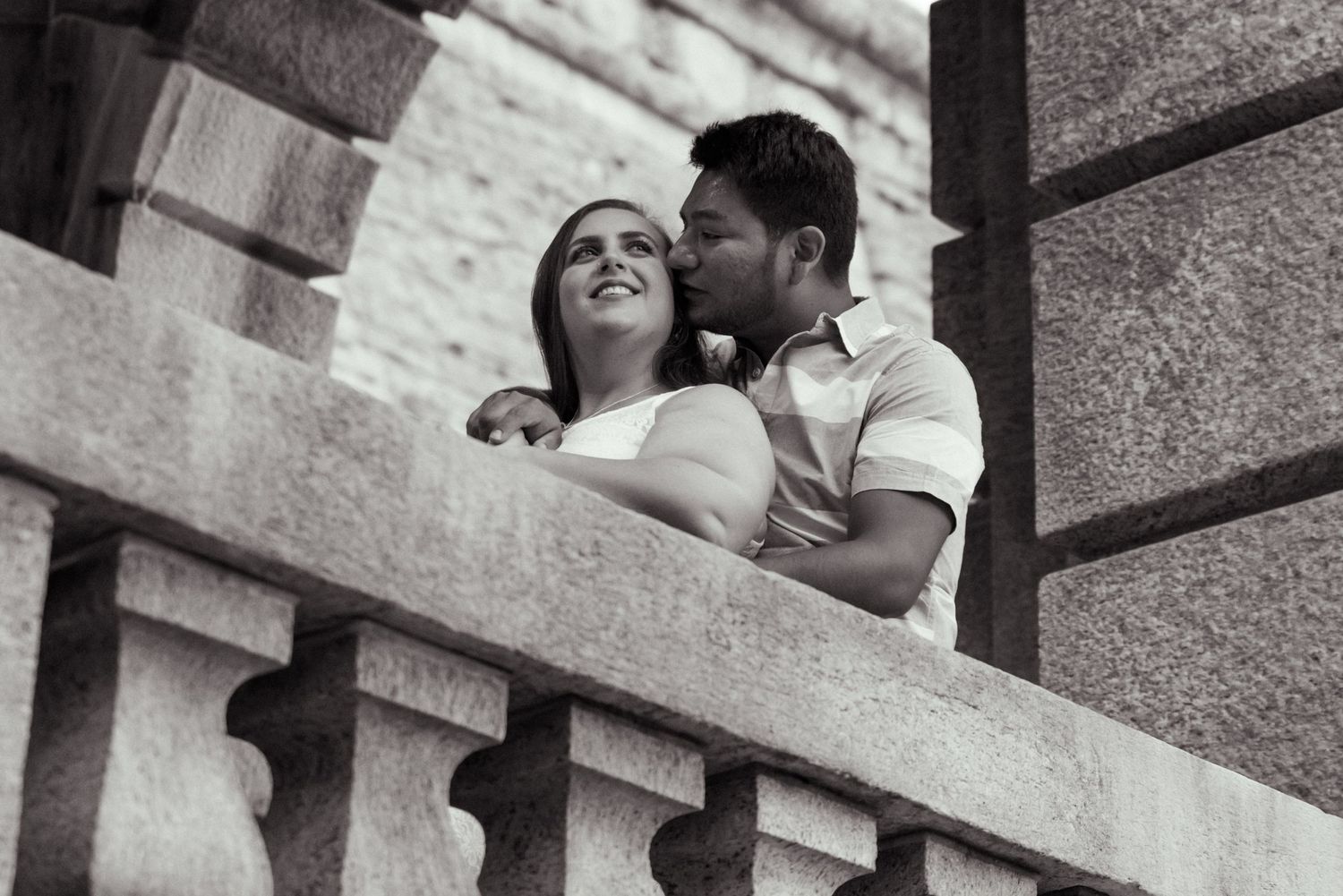 A timeless scene of the groom-to-be holding his future bridge while kissing her on the cheek. The bride looks off into the distance smiling.