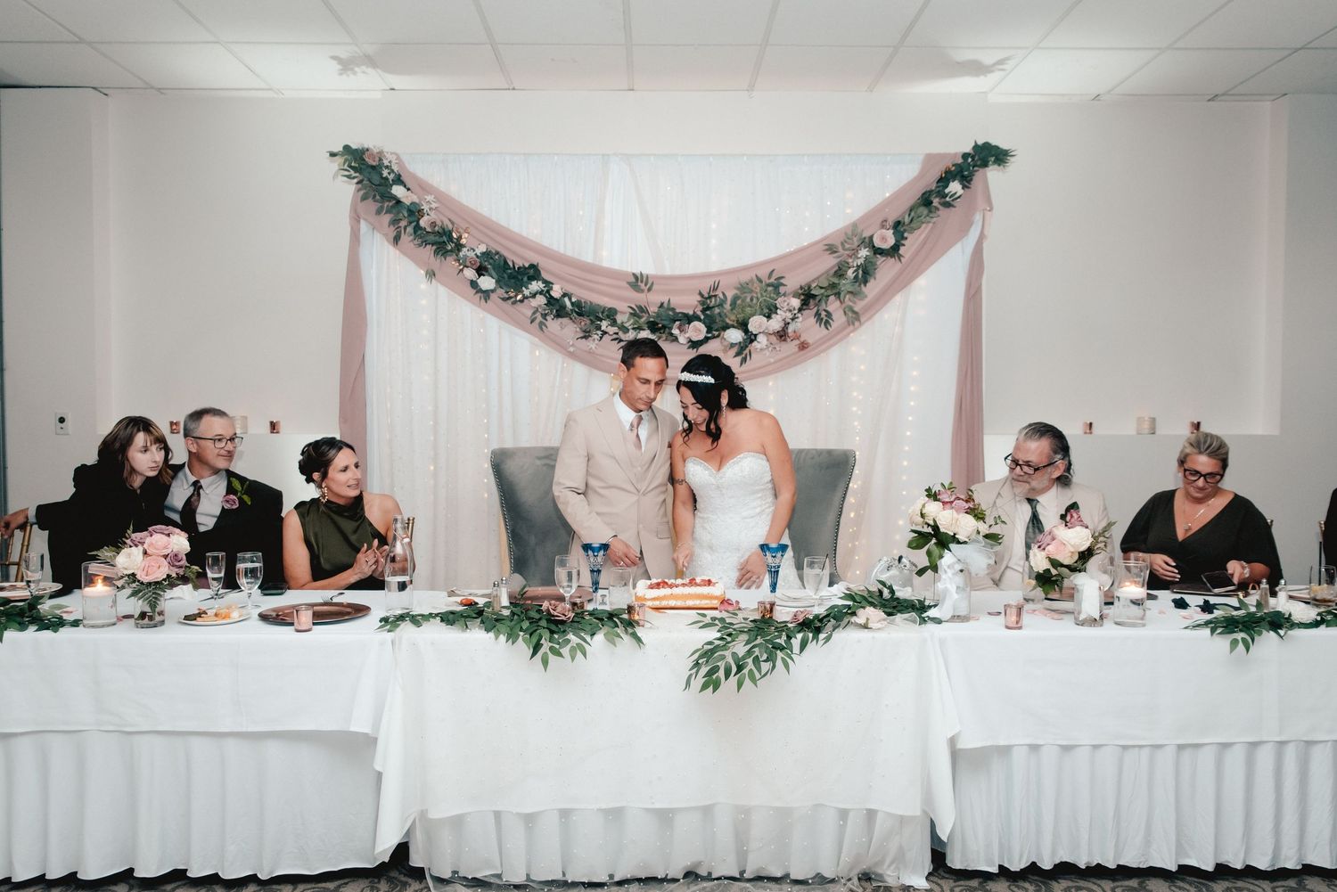 A bridge and groom cut their wedding cake surrounded by the wedding party at the Riverdale in Endicott, NY.