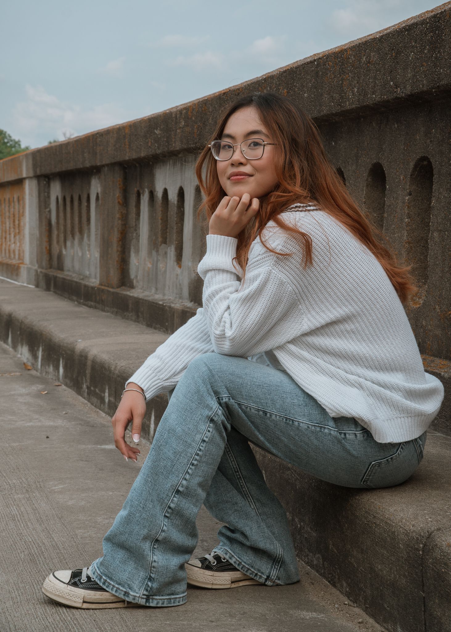 Fashion portraits along a concrete wall wearing jeans and white sweater.