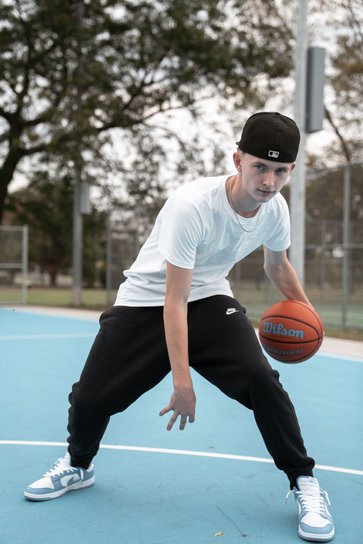 Person in white t-shirt and black pants dribbling a basketball on an outdoor court.