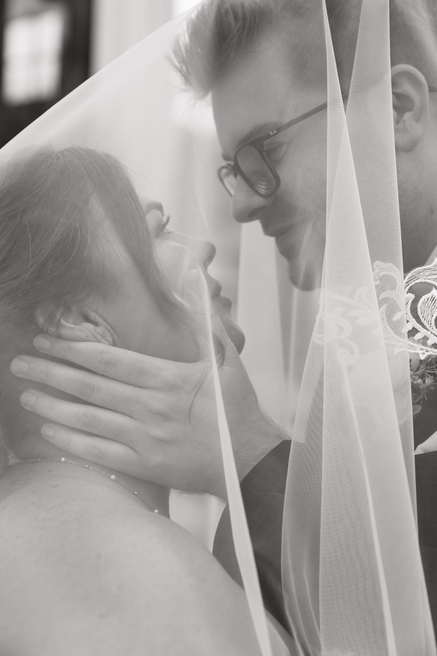 Black and white wedding photo of bride and groom sharing intimate moment under veil.