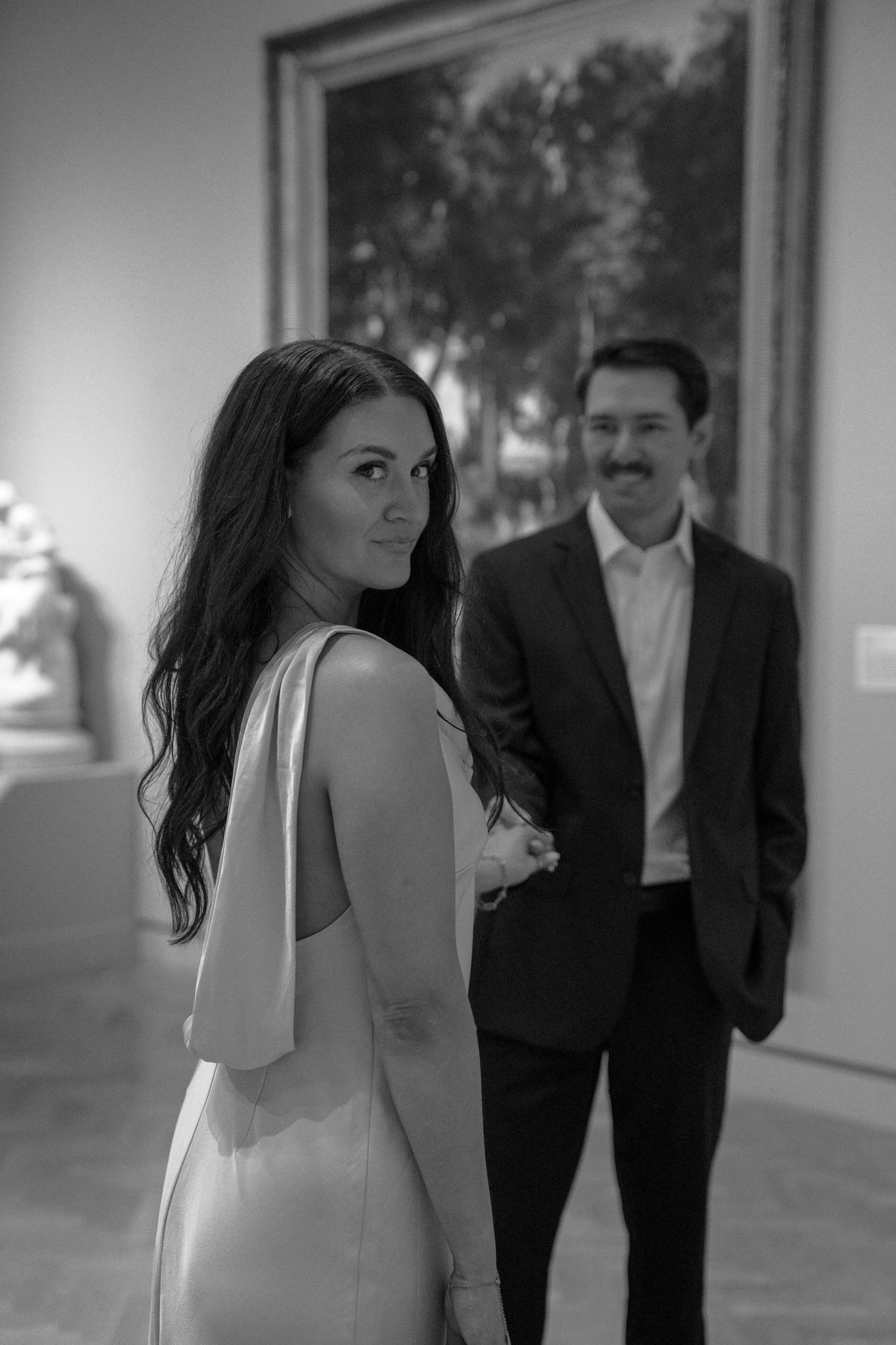 Black and white photo of couple exploring an art gallery with landscape paintings.