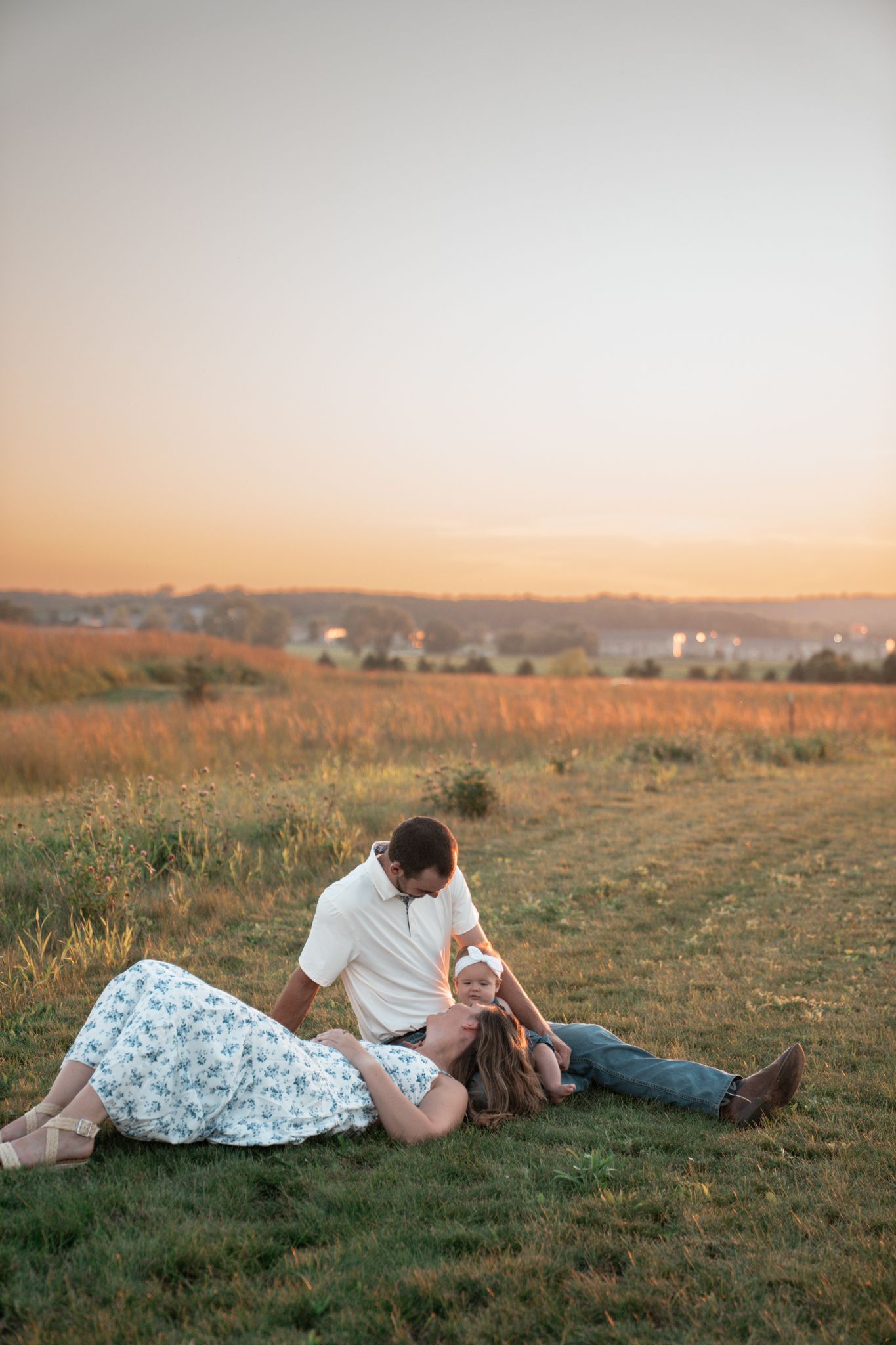 A family relaxes together on grassy hill during golden hour with a scenic countryside backdrop.