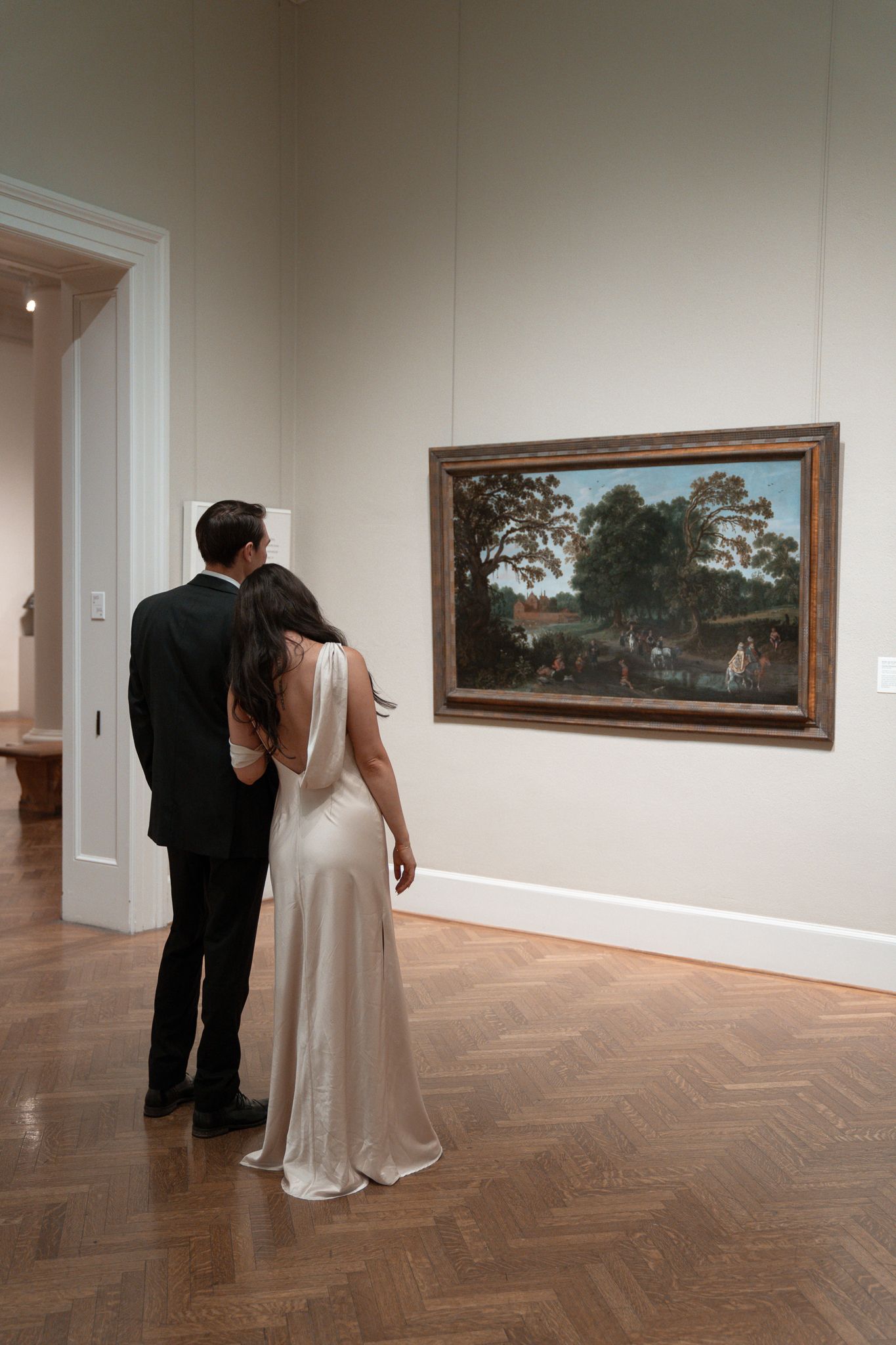 Couple viewing artwork in an elegant museum gallery with herringbone wood floors.