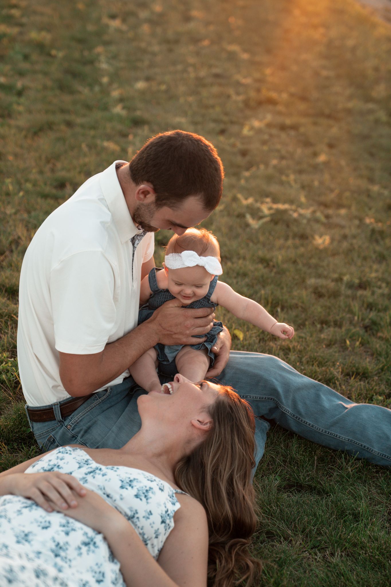 An intimate family moment captured on a grassy hillside during sunset.