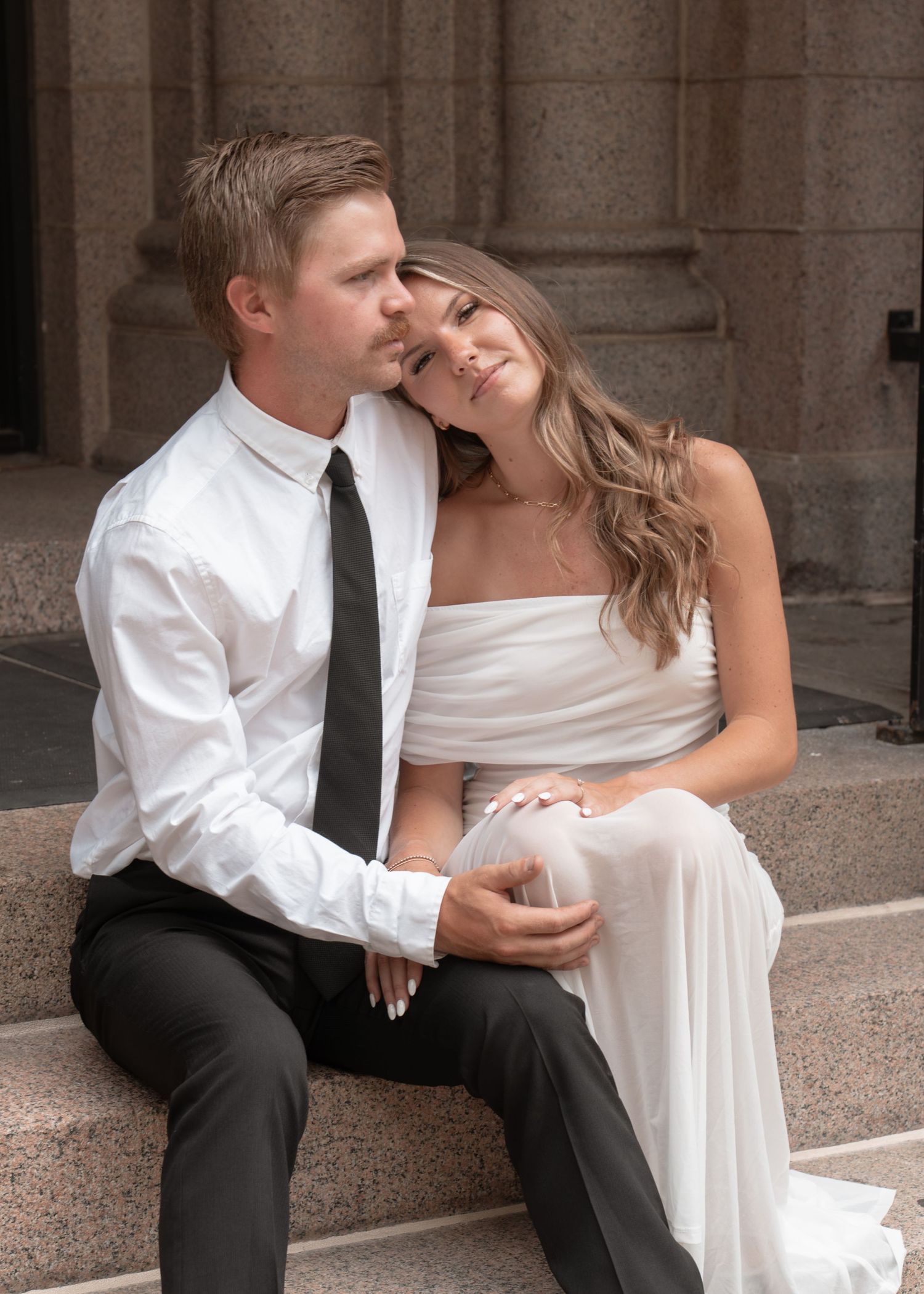 Couple in wedding attire sharing romantic moments on stone steps outdoors.