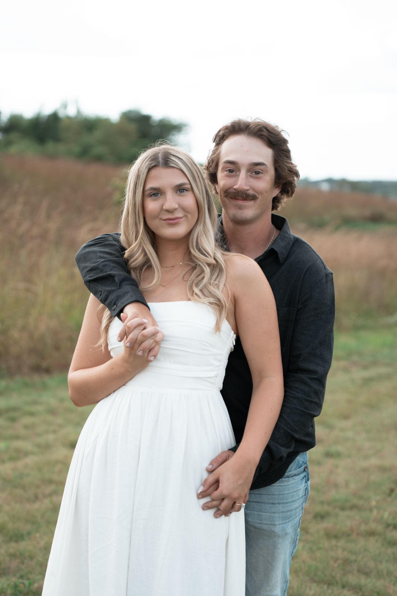 Maternity photo session in a field with white dress and casual attire.