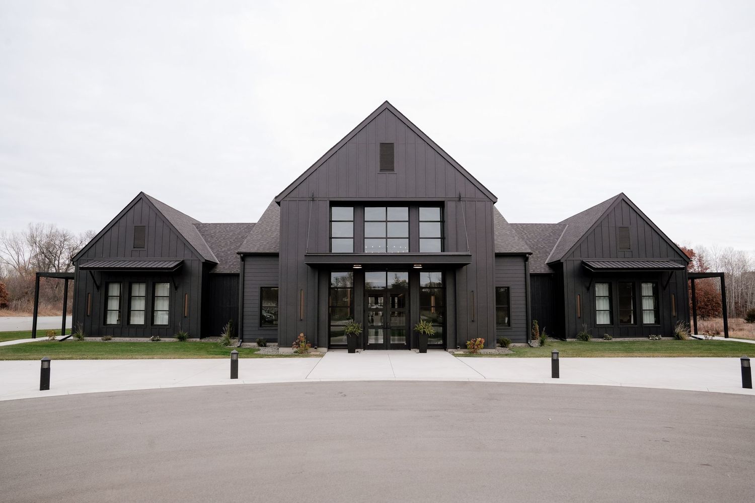 Modern dark gray farmhouse-style building with symmetrical wings and large glass windows features a contemporary architectural design.