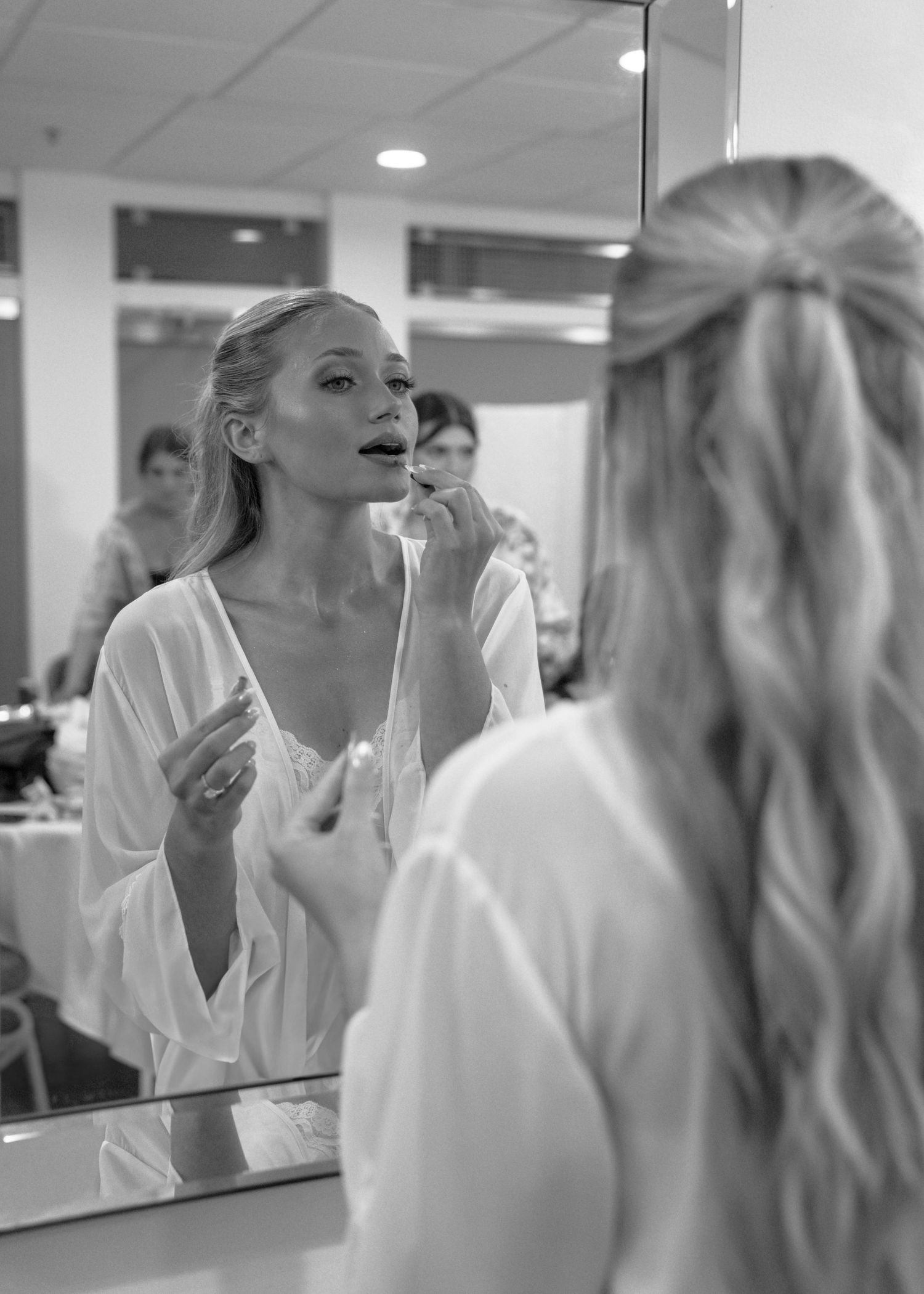 A bride applies lipstick in a photo of mirrored reflections showing the process in black and white photography. Elegant bride, wedding photo