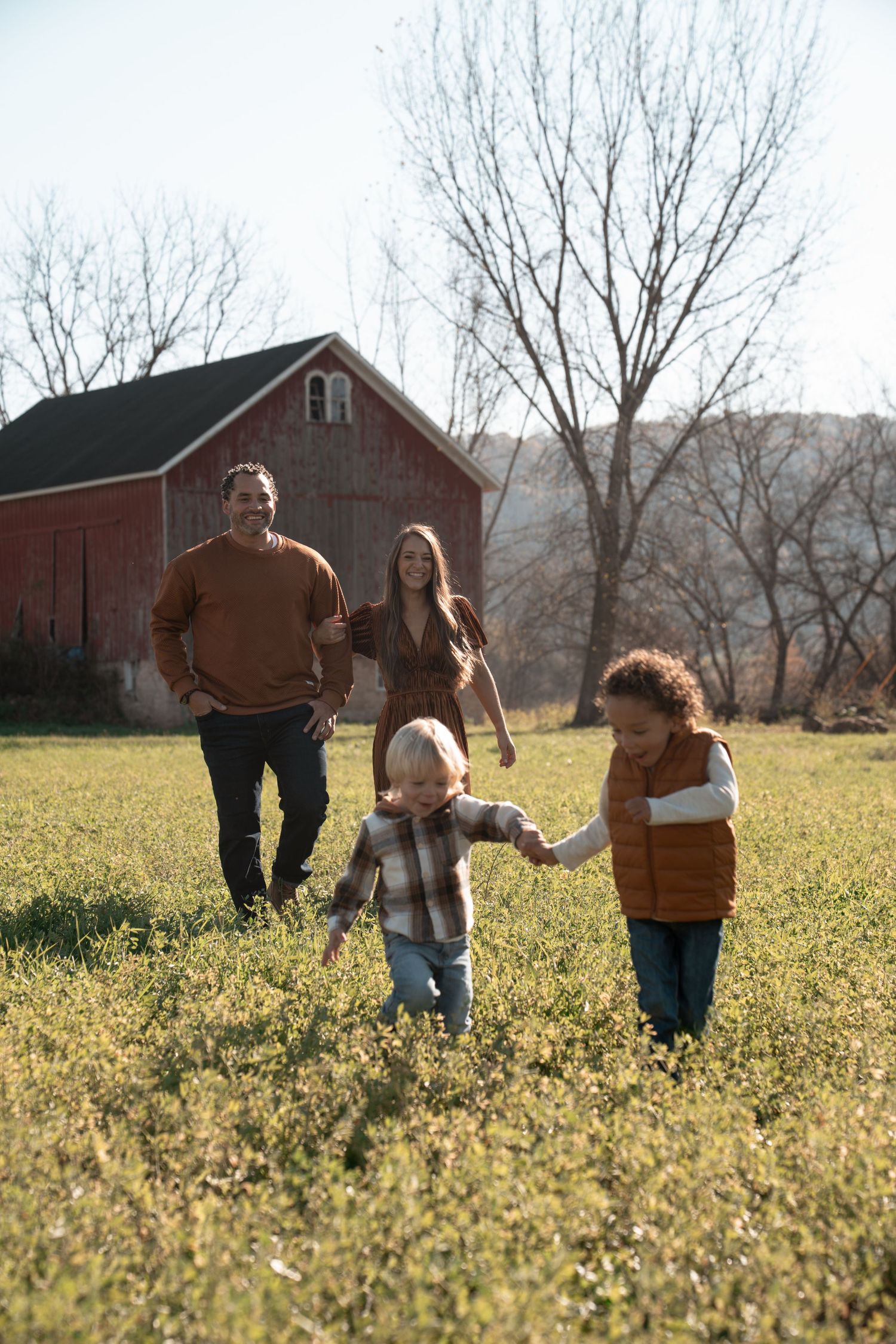 A group walks together through a sunlit field of yellow wildflowers with a red barn in the background.
