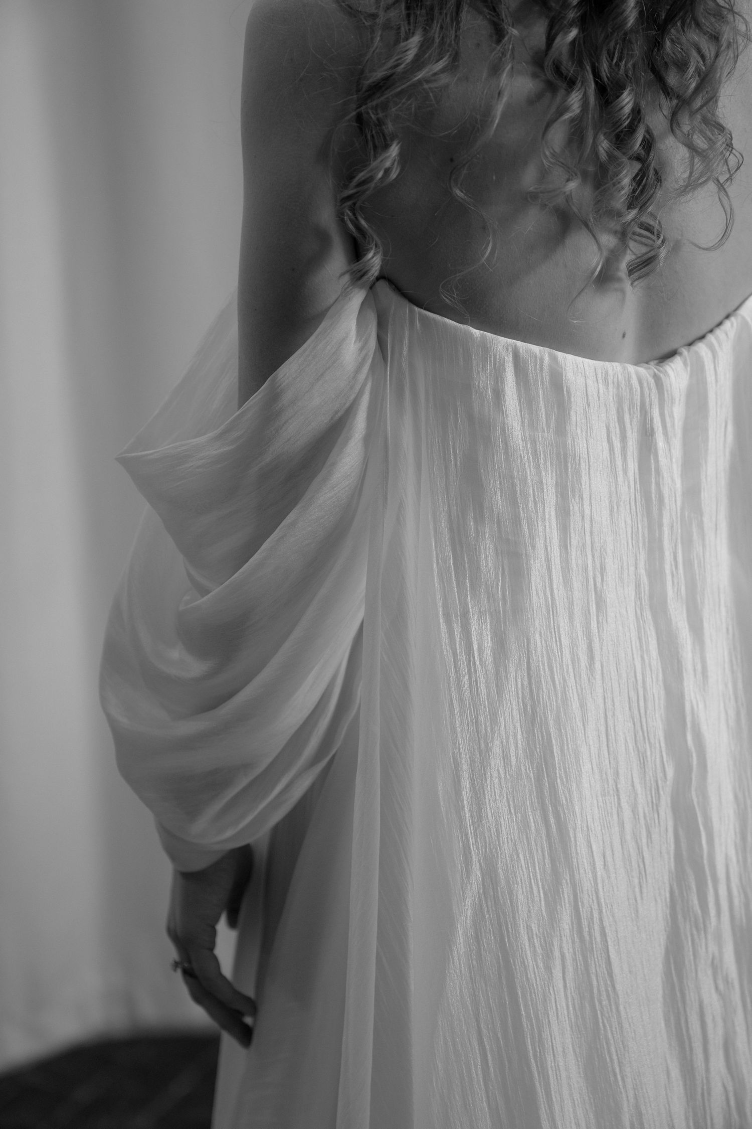 Black and white artistic photograph showing flowing white fabric draping off shoulders with delicate pleats and texture. Mayowood Stonebarn.