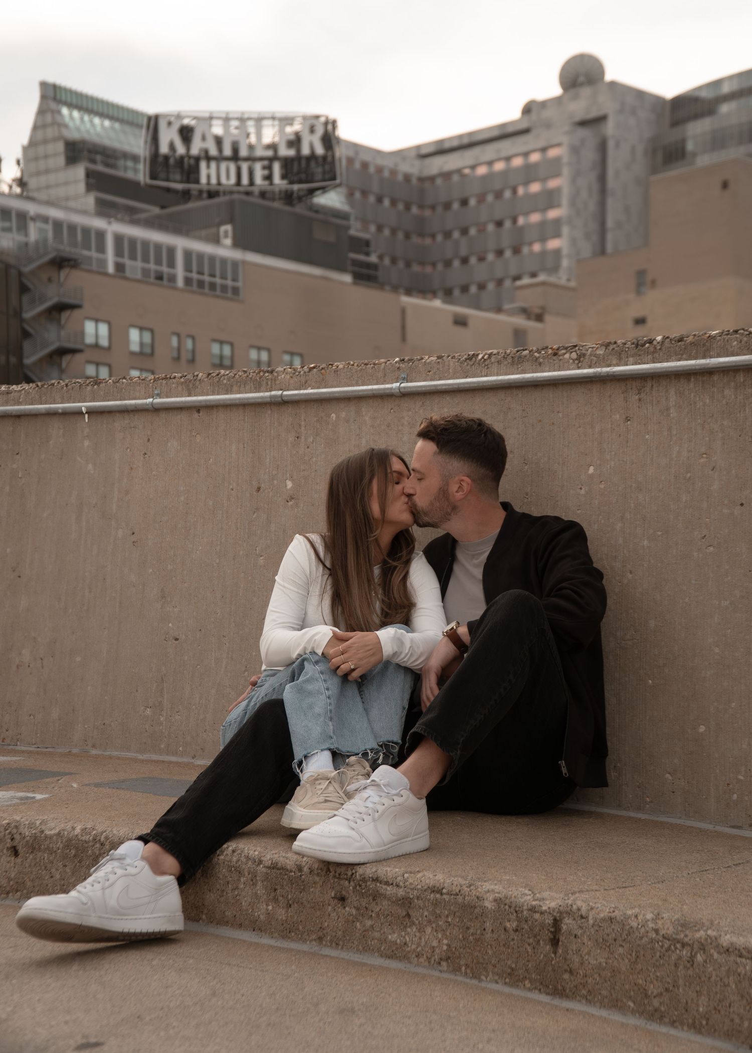 A couple lounges together on concrete steps against an urban backdrop.