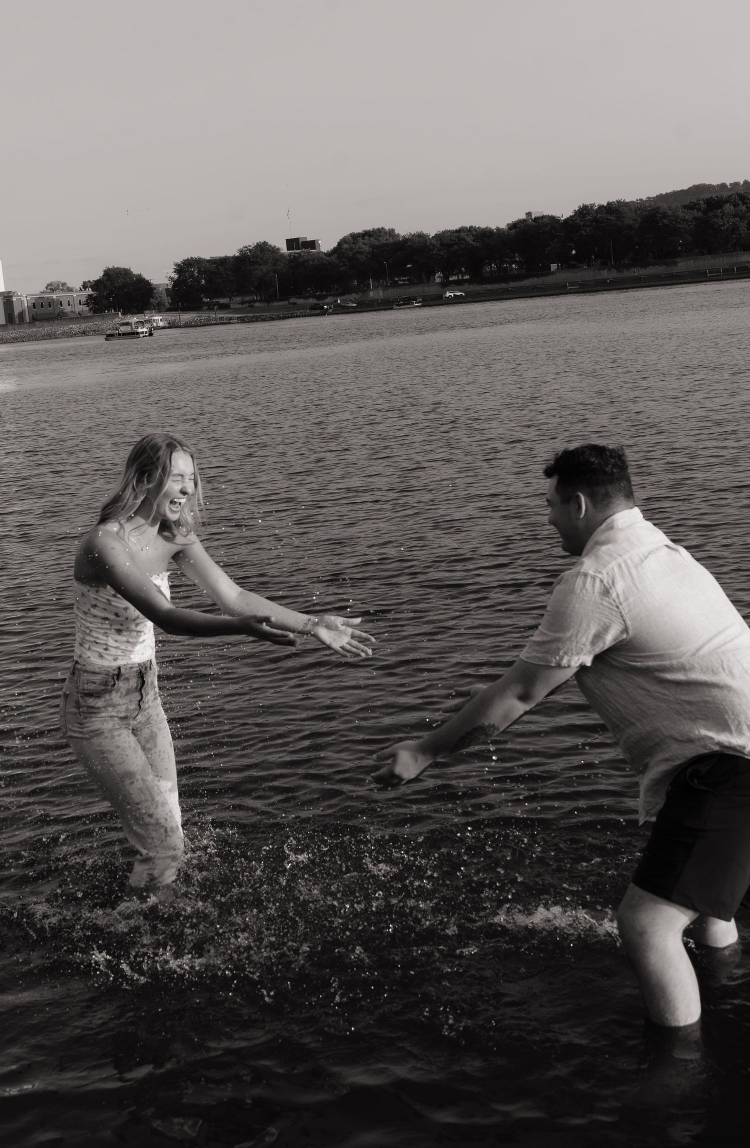 Black and white photo of a couple playfully splashing water at each other while standing in a lake.