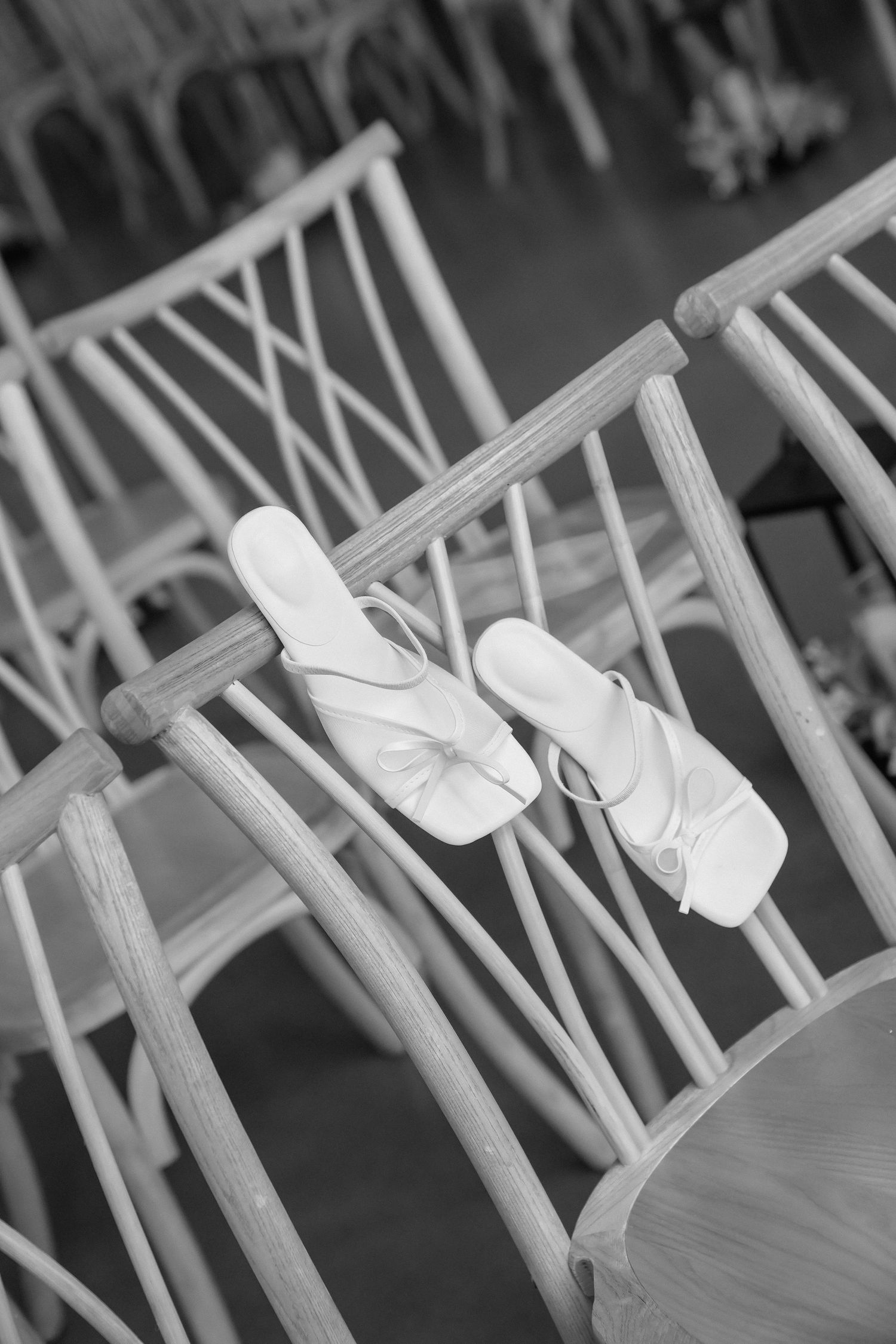White ballet slippers hanging on a wooden chair at a wedding venue.