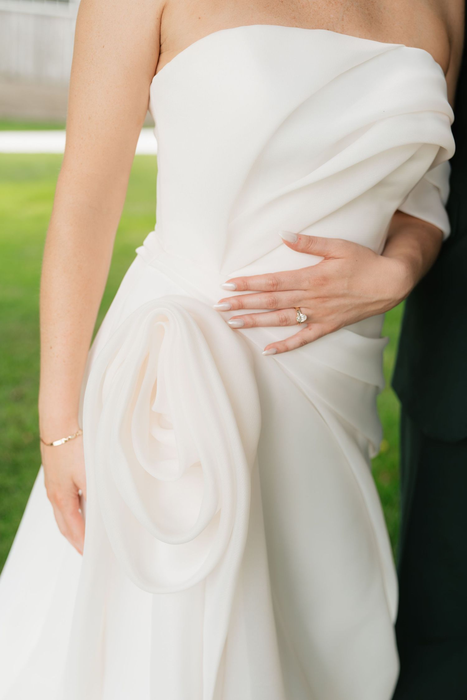 Close-up of bride in strapless white wedding gown with elegant draping, wearing diamond ring and gold bracelet.