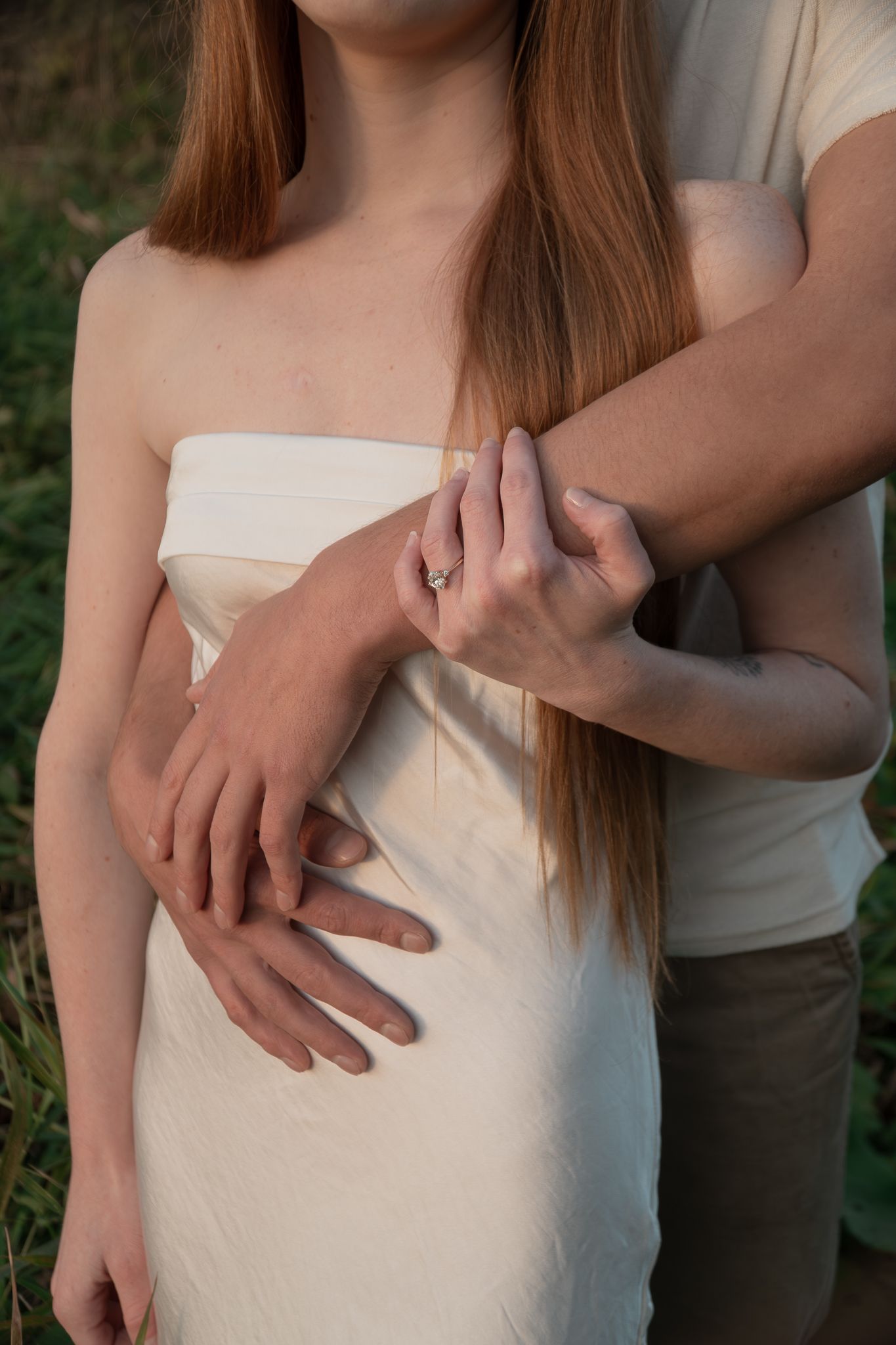 Close up of hands embracing around a white dress in golden sunlight.
