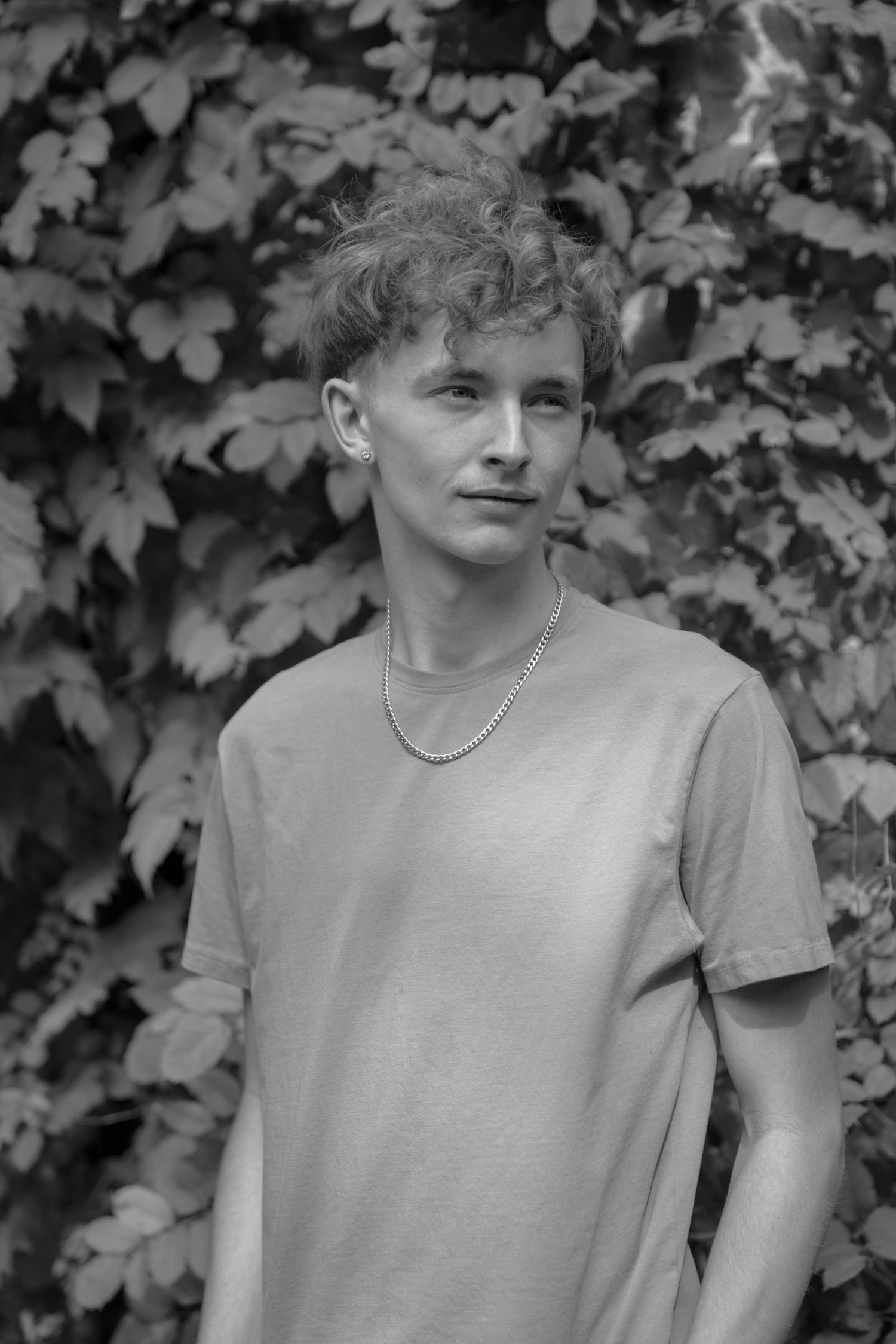 Black and white portraits showing person in casual attire against leafy background.