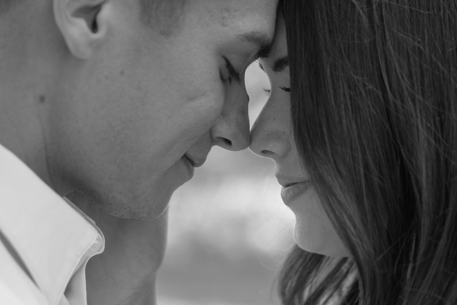 Black and white romantic photo of a couple leaning foreheads together, sharing an intimate moment.