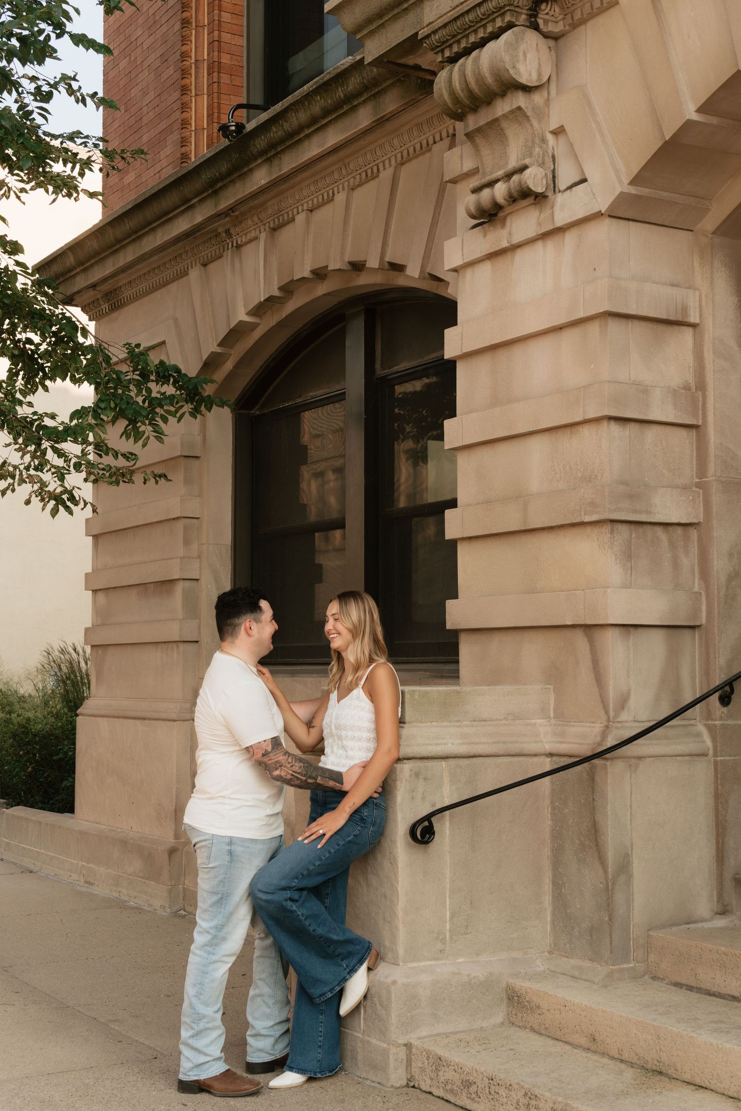 Couple sharing a romantic moment outside a historic sandstone building with arched windows and ornate details.