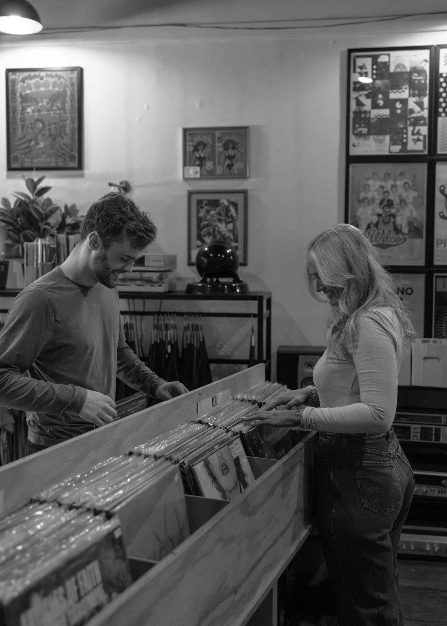 A couple browses through vinyl records together in a record store with framed artwork on the walls.