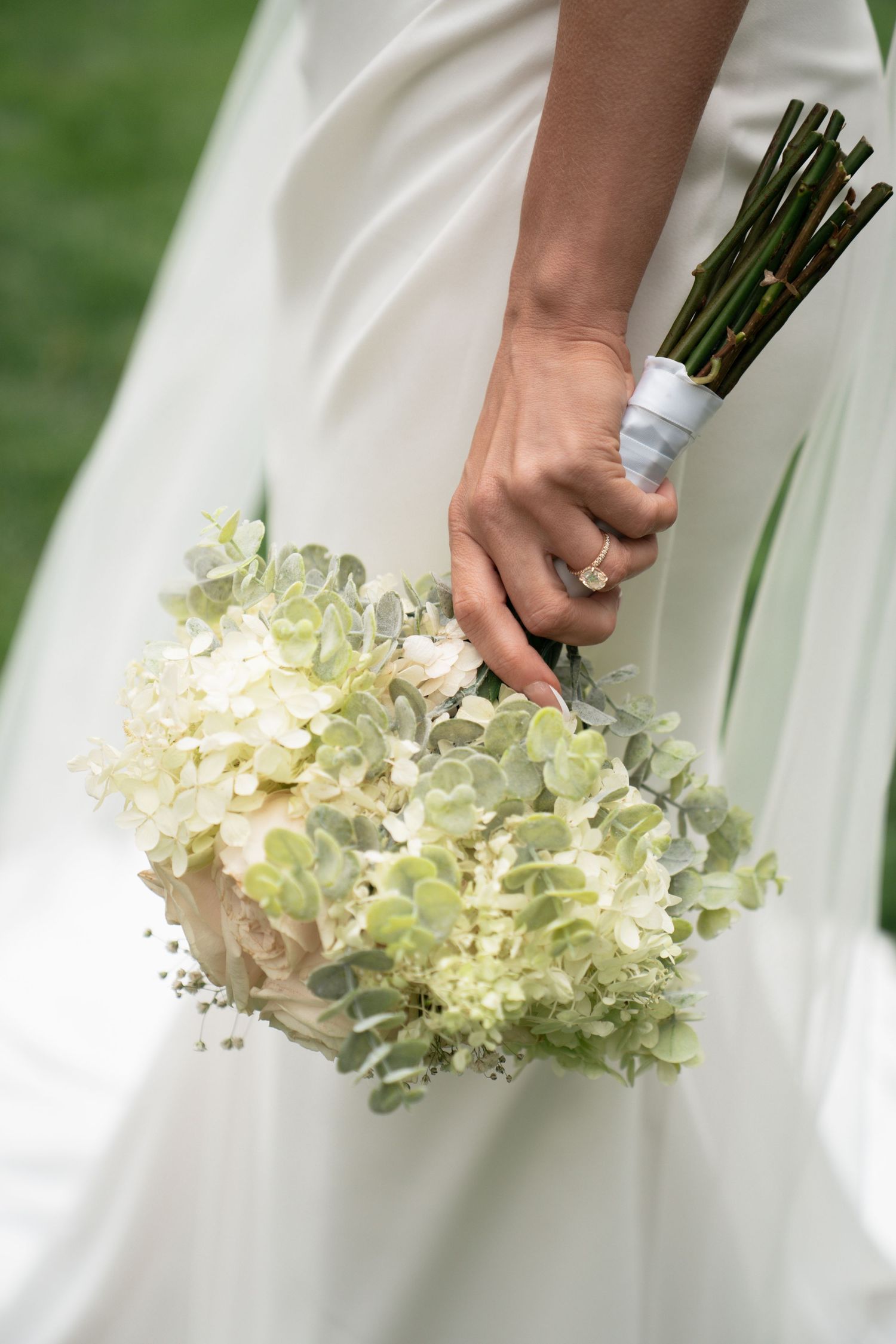 A wedding bouquet of white hydrangeas is held against flowing white fabric, creating an elegant bridal detail shot. Byron, MN wedding.