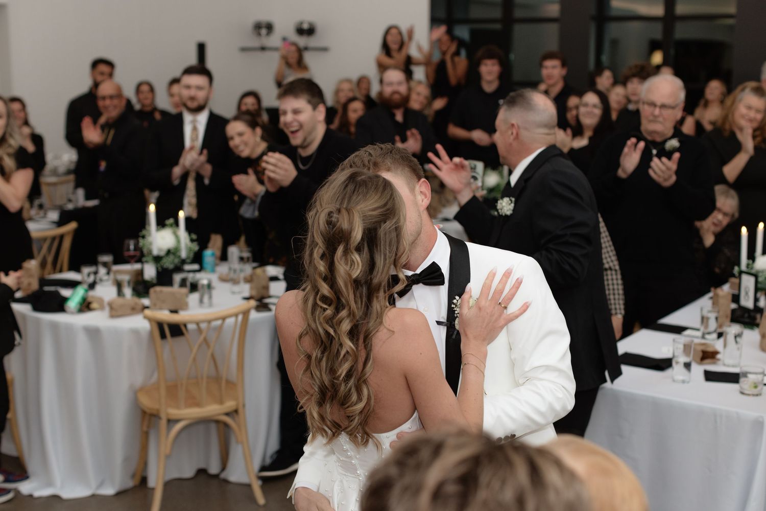 A couple shares a romantic dance together at an elegant wedding reception with guests seated at tables in the background.
