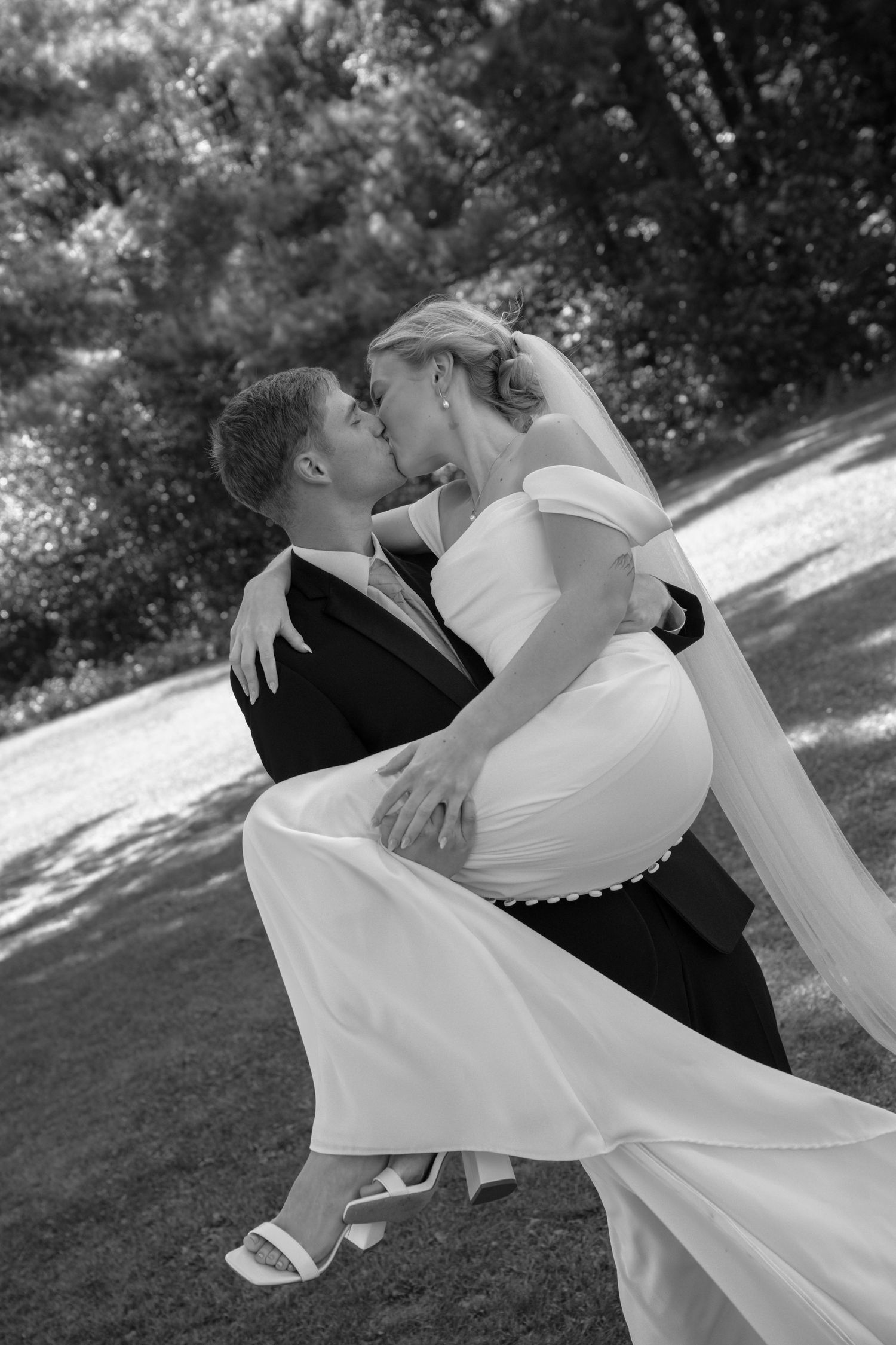 A romantic black and white wedding photo of a couple dancing outdoors in formal attire.