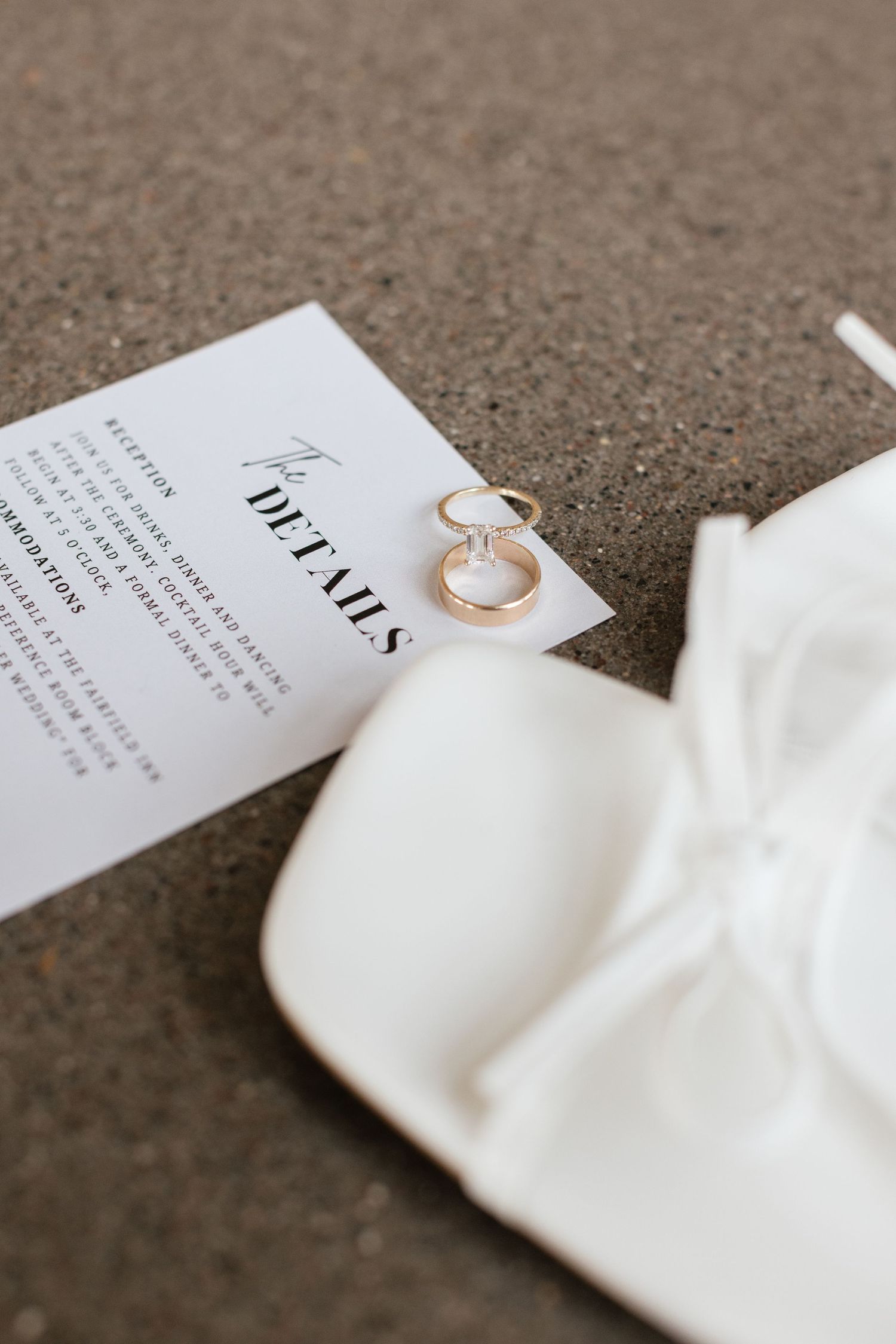 Wedding invitation details and engagement ring on white fabric against a textured gray surface. Wedding details, flat-lay. Engagement ring.
