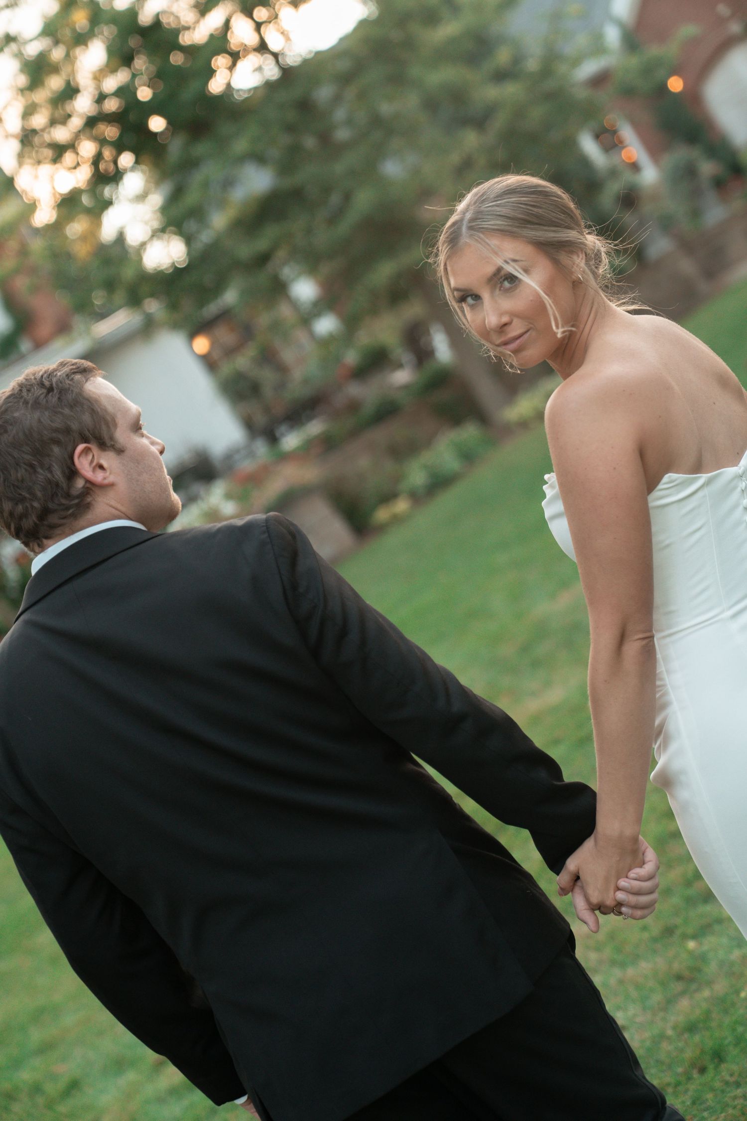 A sequence of photos shows a couple in wedding attire playfully falling onto grass during their outdoor photo session.