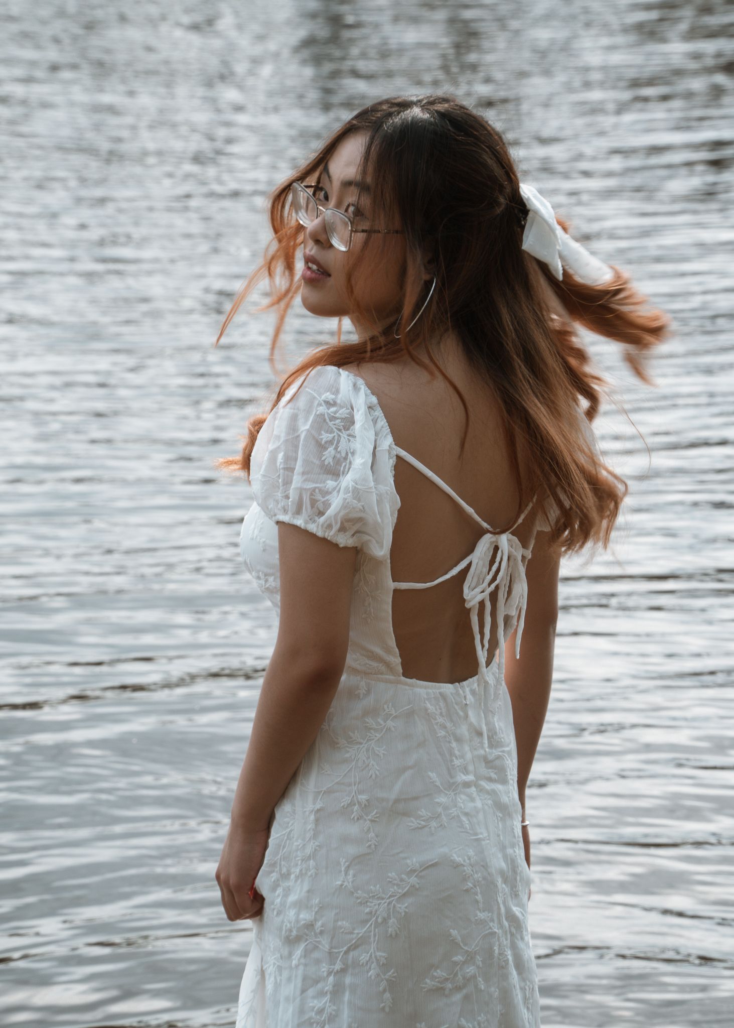 Side view portraits in a white dress near water with movement and natural light.