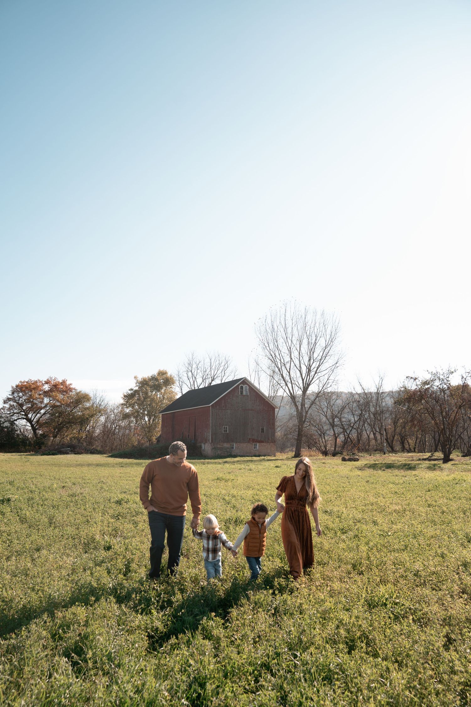 People stroll through a pastoral meadow with a rustic red barn visible in the distance.