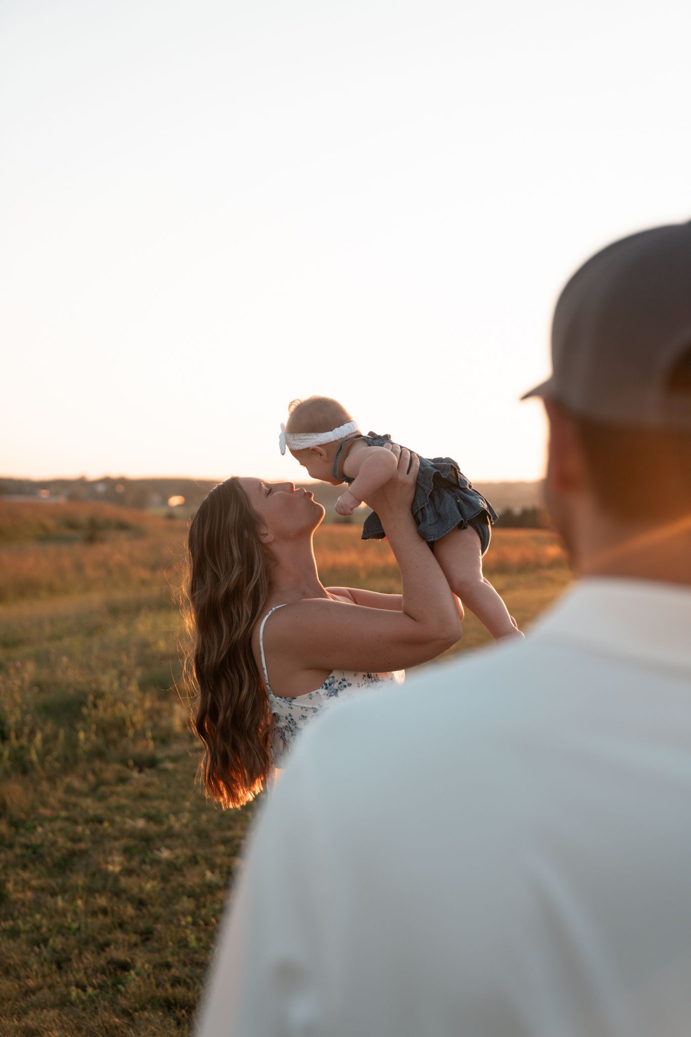 A heartwarming sunset scene of a baby being lifted high in the air in an outdoor setting.