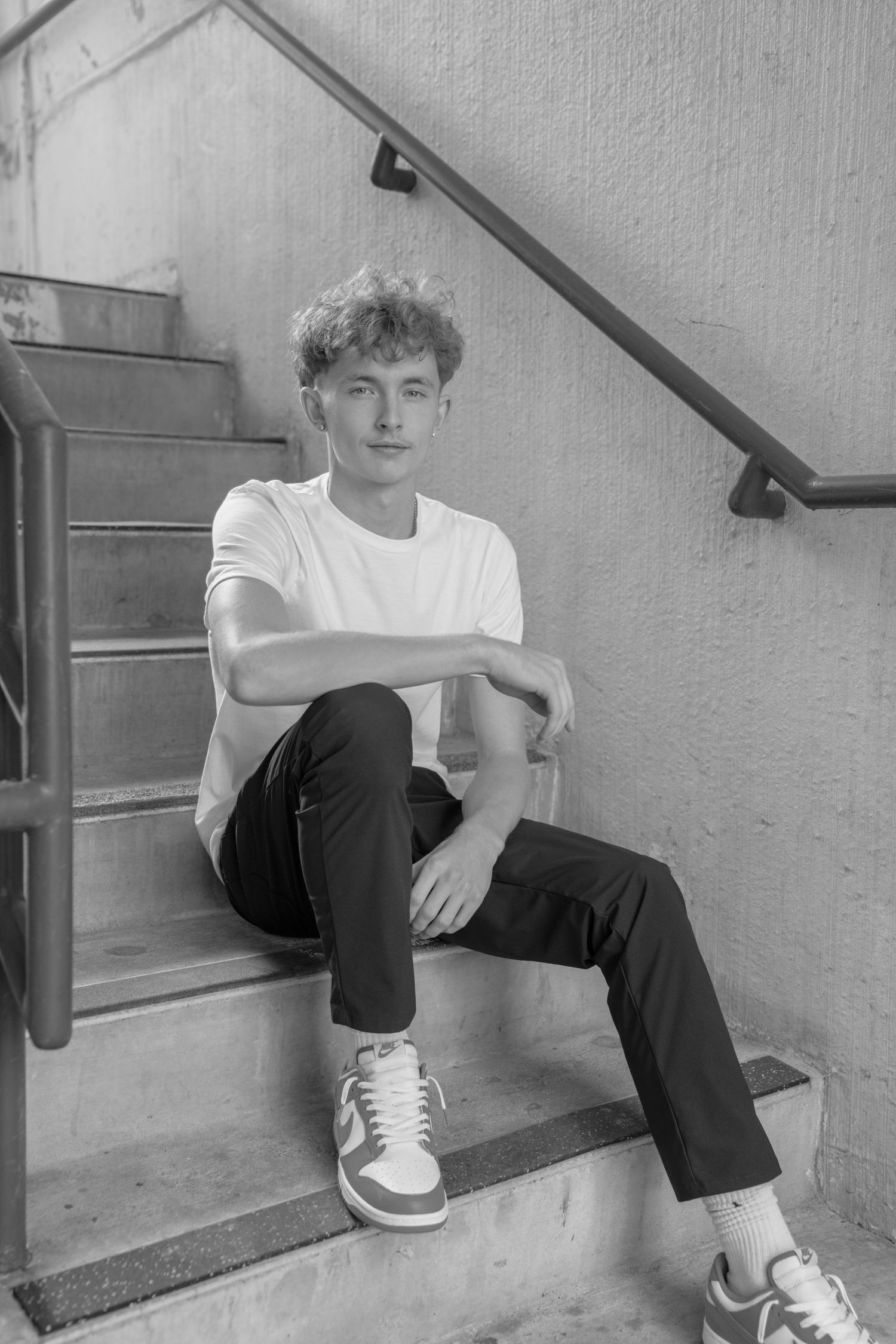 Black and white photos of someone sitting on concrete steps wearing sneakers and casual clothes.