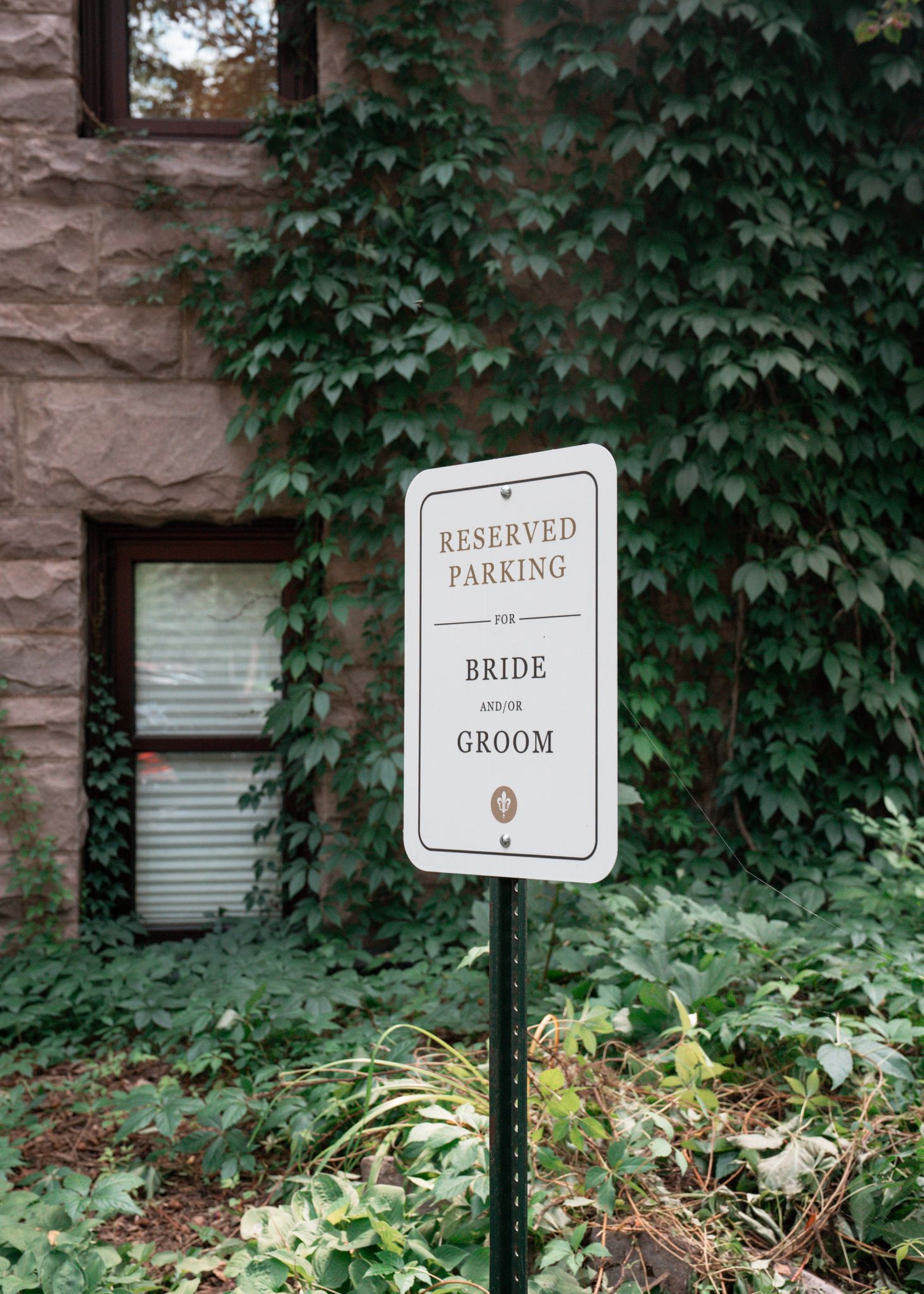 White reserved parking sign for a bride and groom mounted on posts among green ivy-covered walls. Minneapolis, MN.