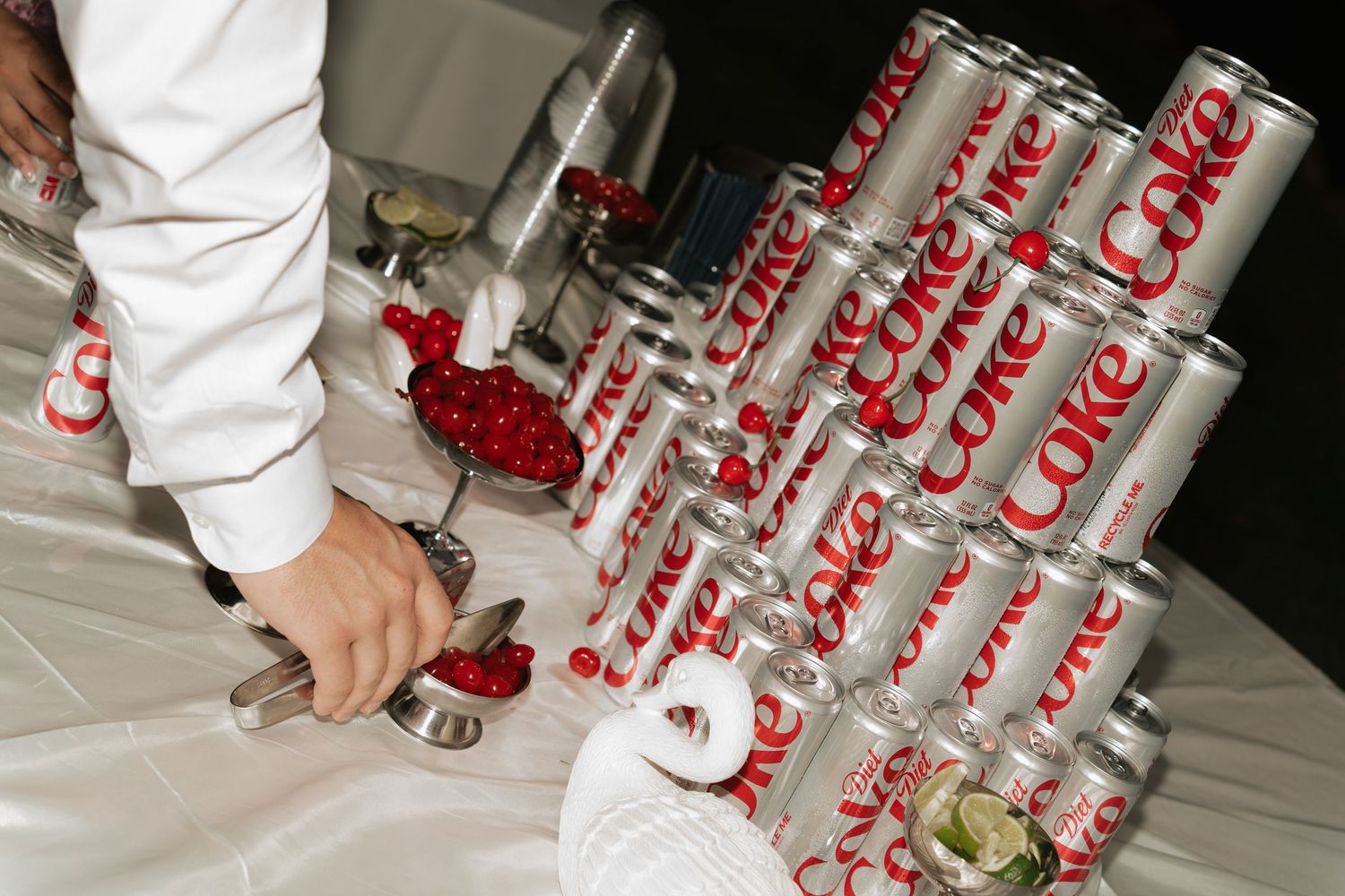Diet Coke cans stacked in a pyramid display at a catered event with a server using tongs nearby.