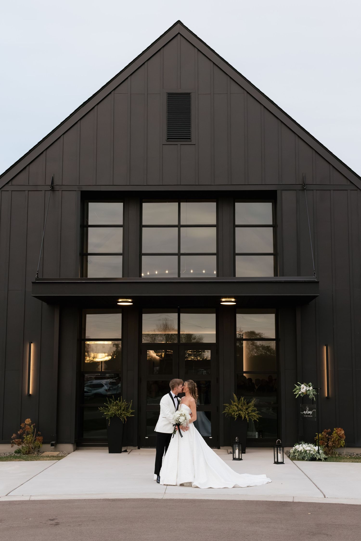 Bride and groom sharing a romantic kiss outside a modern black barn wedding venue at dusk.